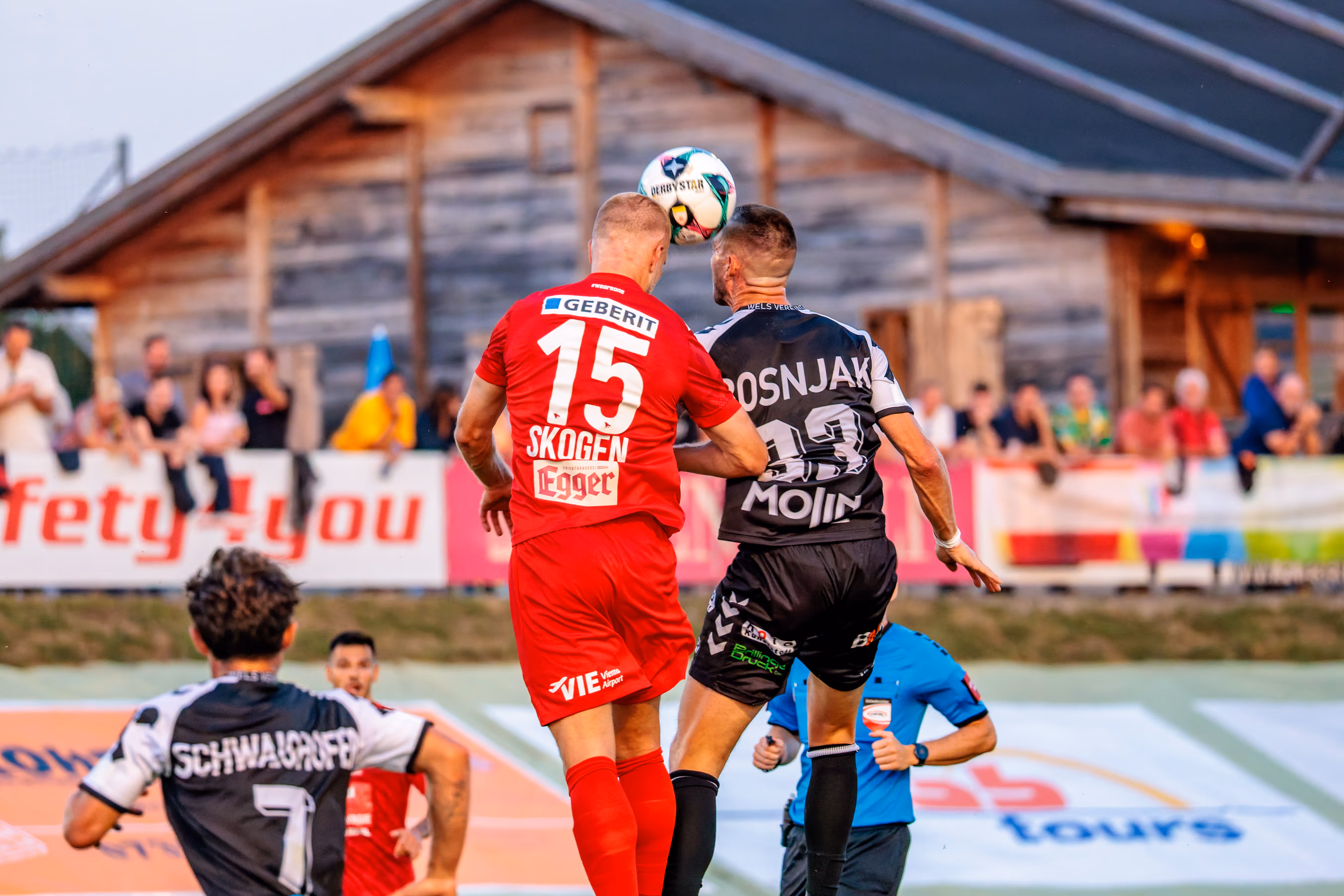 Ein Spieler von SPG HOGO Wels im roten Trikot und ein Spieler von SKN St. Pölten im schwarz-weißen Trikot liefern sich ein intensives Kopfballduell im ÖFB-Cup