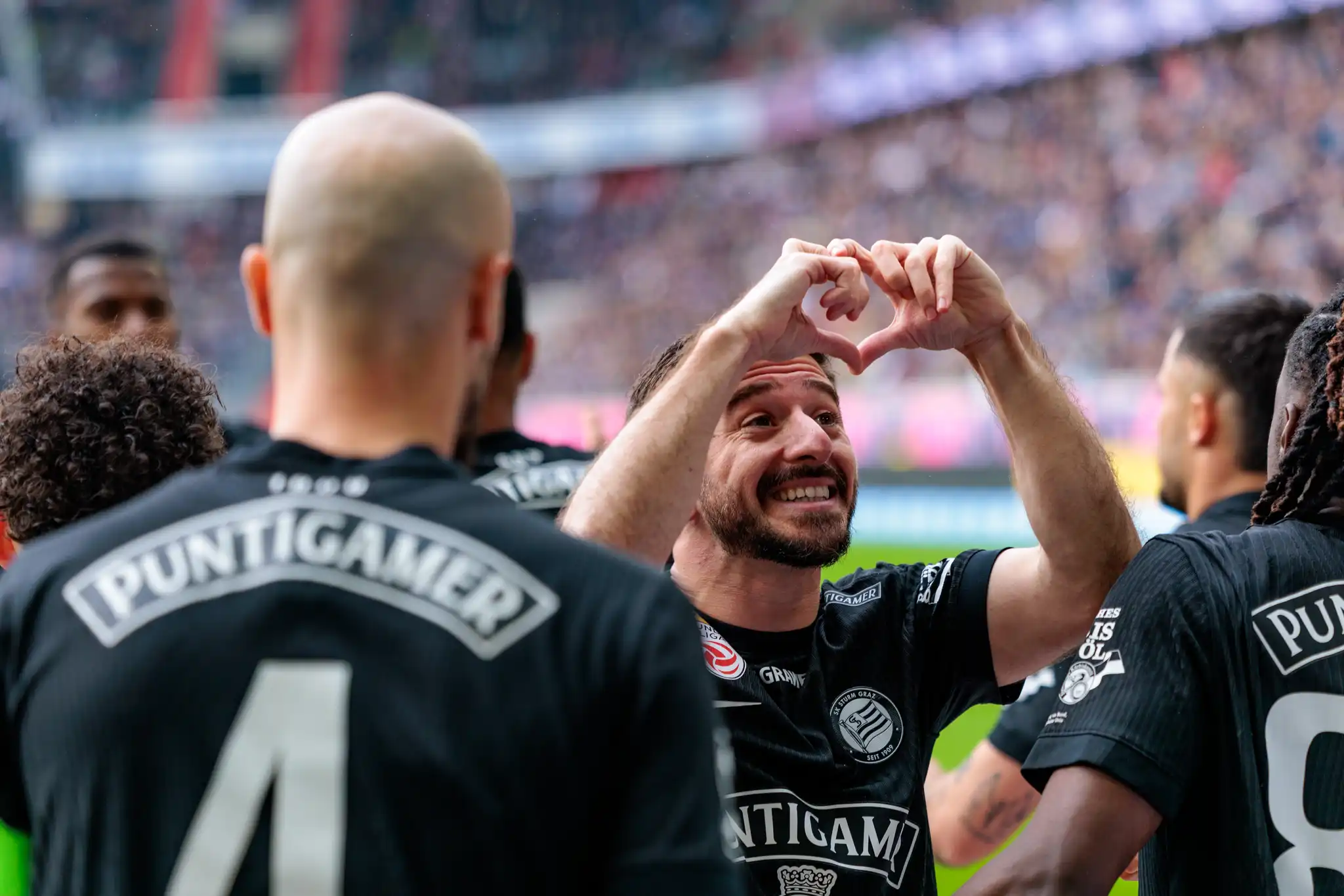 Ein lächelnder Spieler von Sturm Graz formt mit seinen Händen ein Herz als Torjubel vor den Zuschauern