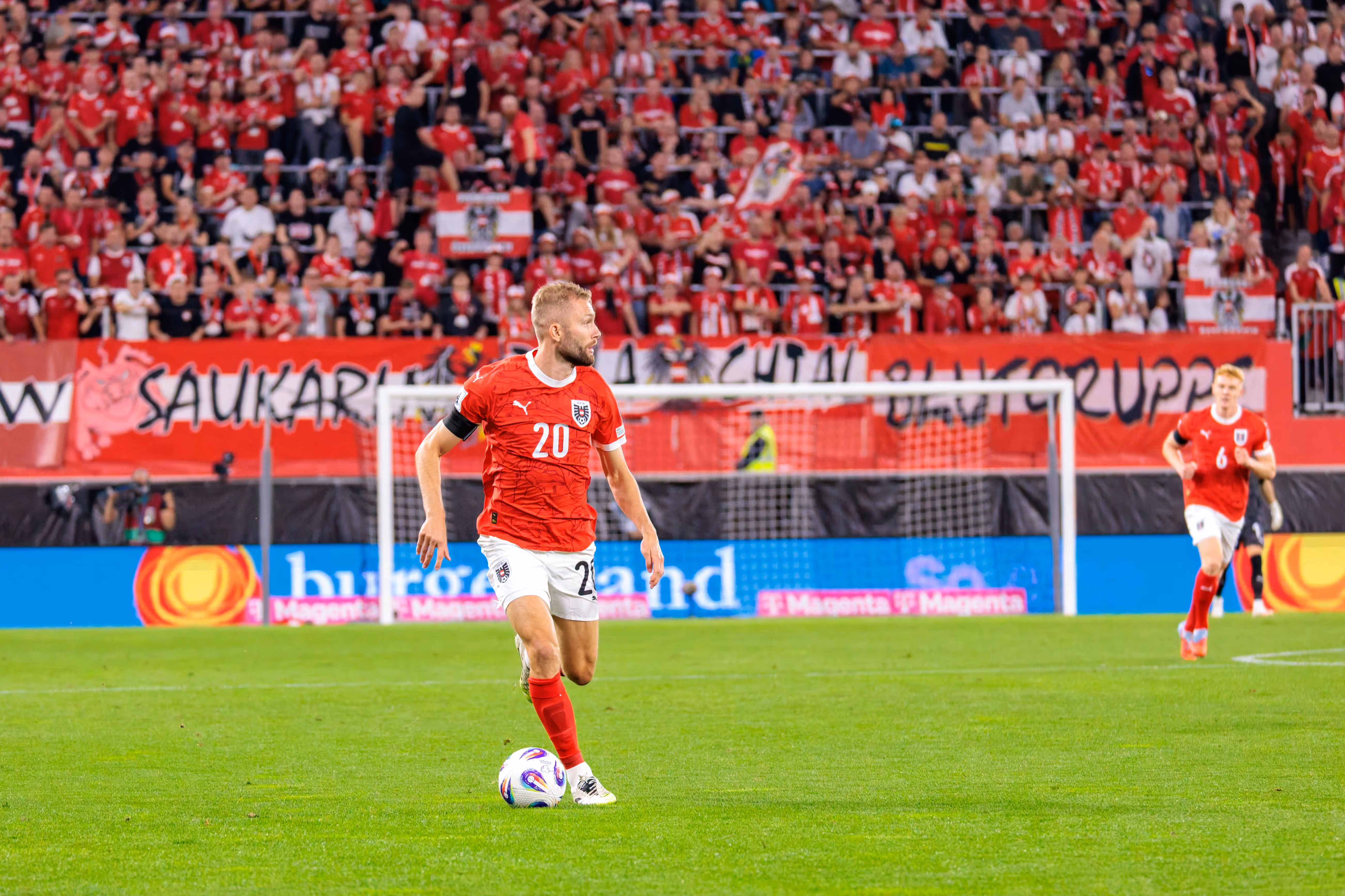 Der österreichische Nationalspieler Konrad Laimer mit der Trikotnummer 20 dribbelt den Fußball auf dem Spielfeld während des WM-Qualifikationsspiels gegen Zypern vor einer unscharfen Zuschauerkulisse