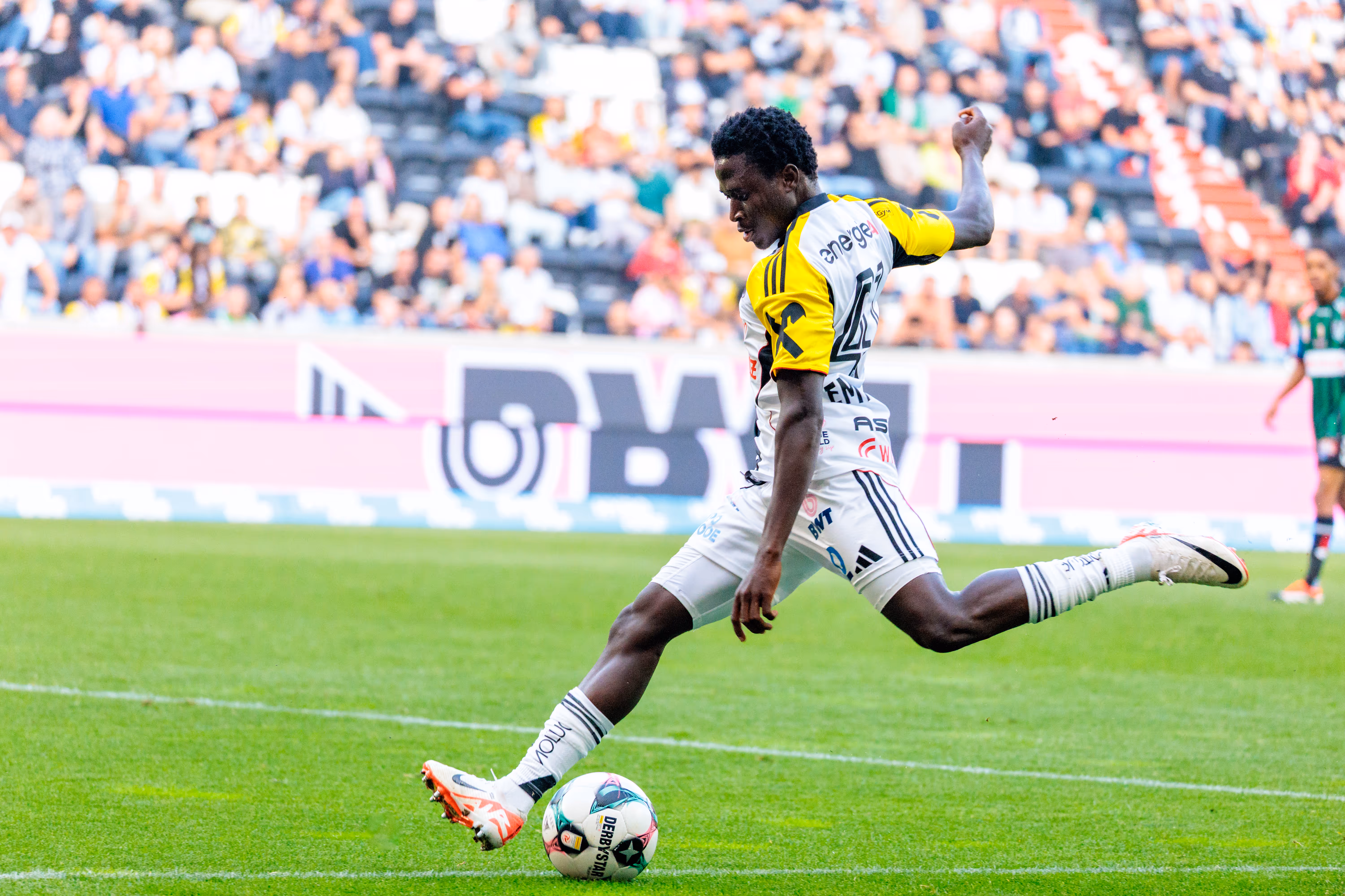 Ein LASK-Spieler in weiß-gelbem Trikot flankt den Ball während eines Bundesliga-Spiels