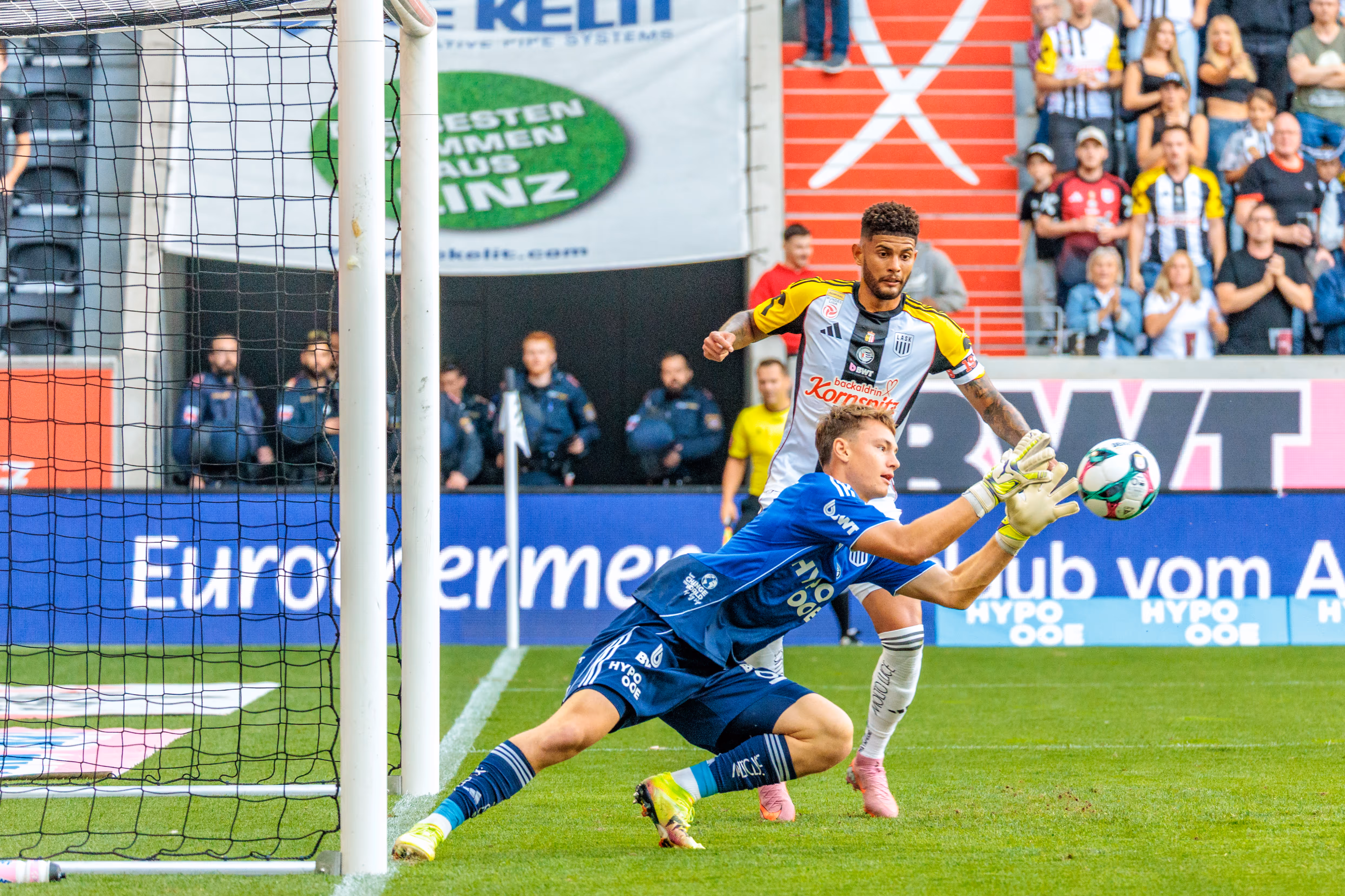 Lukas Jungwirth im blauen Trikot pariert einen Fußball mit einer Hechtparade während eines Bundesliga-Spiels