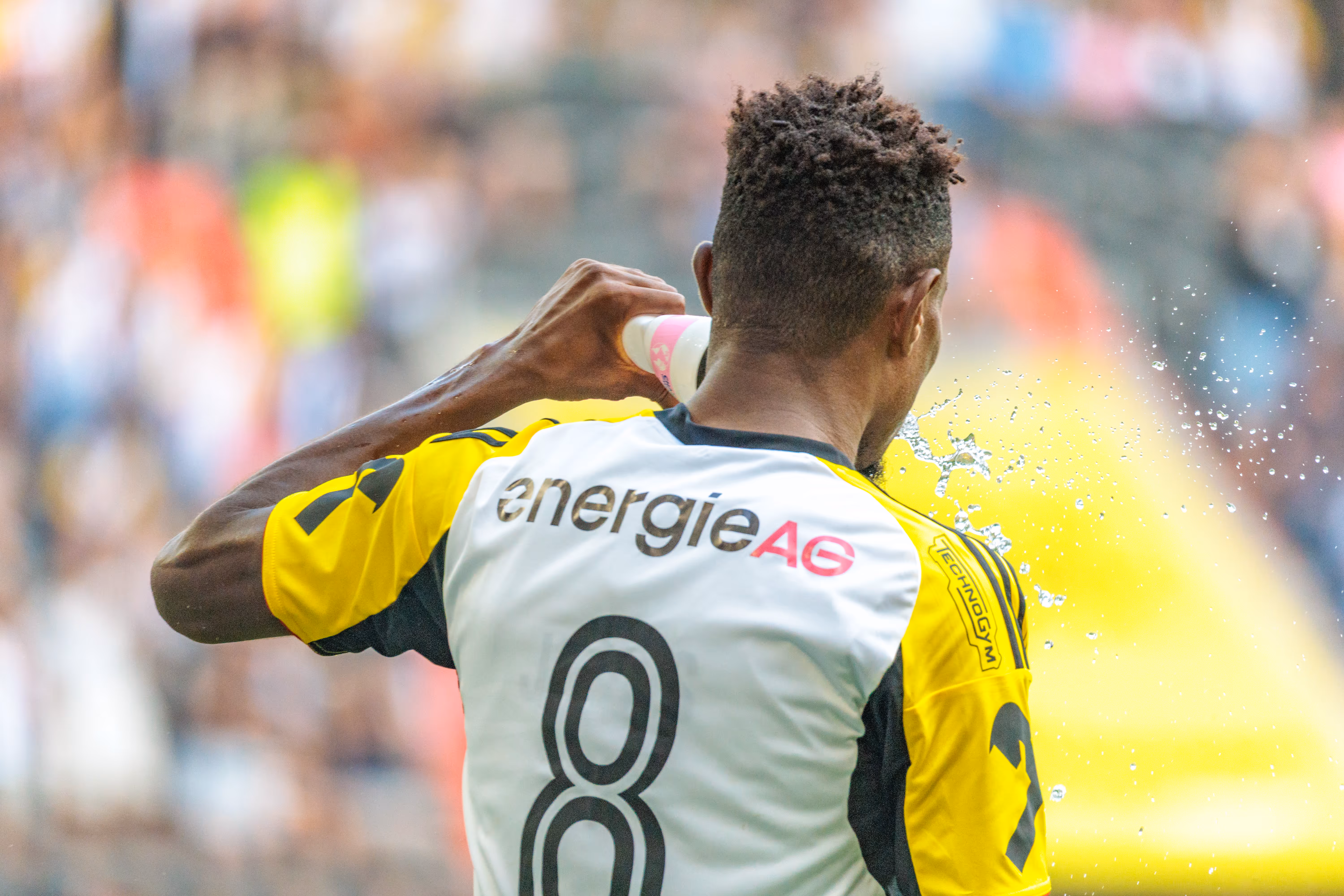 Der LASK-Spieler Moses Usor mit der Rückennummer 8 auf seinem weiß-gelben Trikot erfrischt sich während eines Fußballspiels durch das Spritzen von Wasser aus einer Flasche
