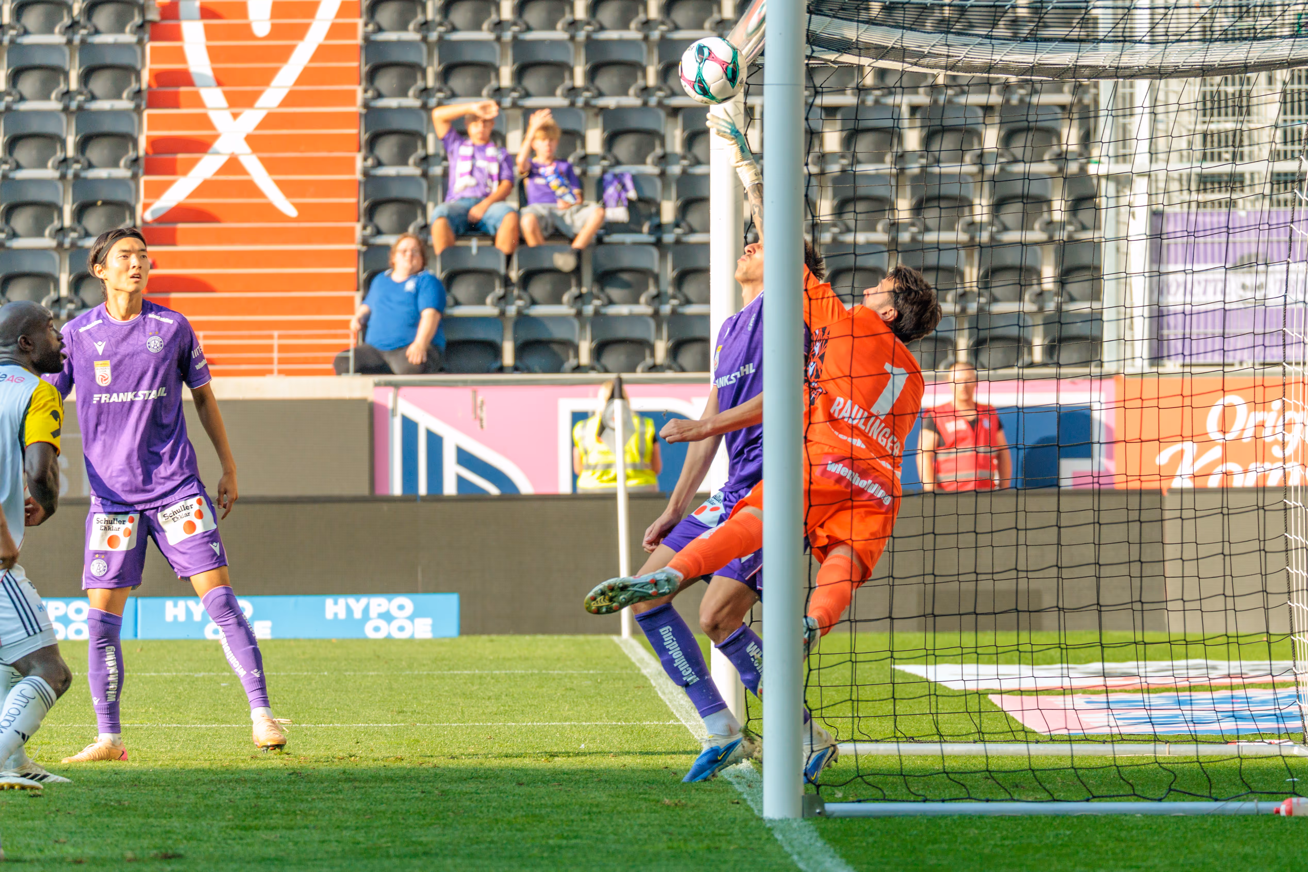 Ein Torhüter der Austria Wien in orangefarbenem Trikot pariert einen Schuss des LASKs nahe der Latte