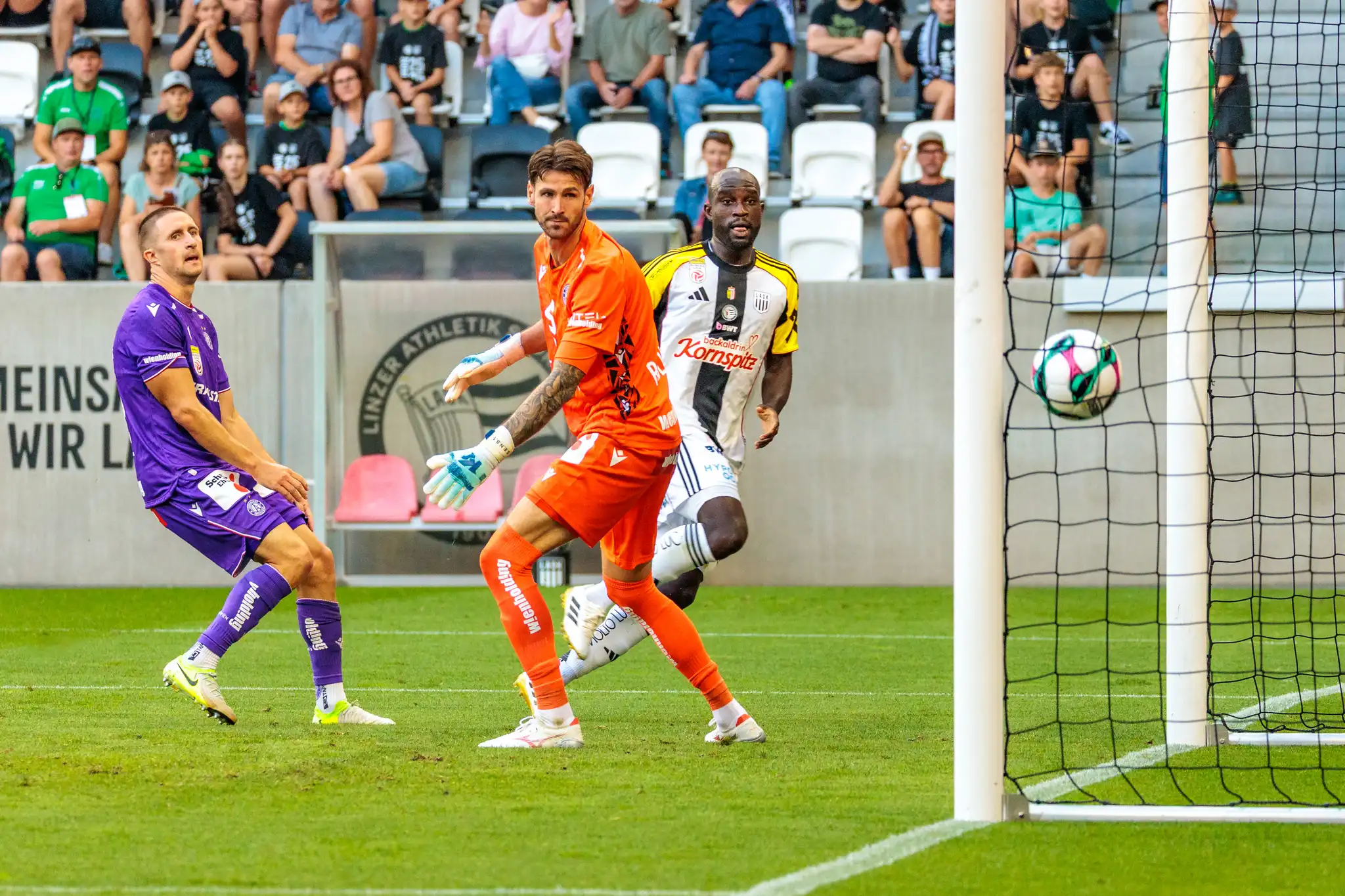Der Ball liegt im Tornetz, während Fußballspieler des LASK und von Austria Wien auf das soeben erzielte Tor blicken
