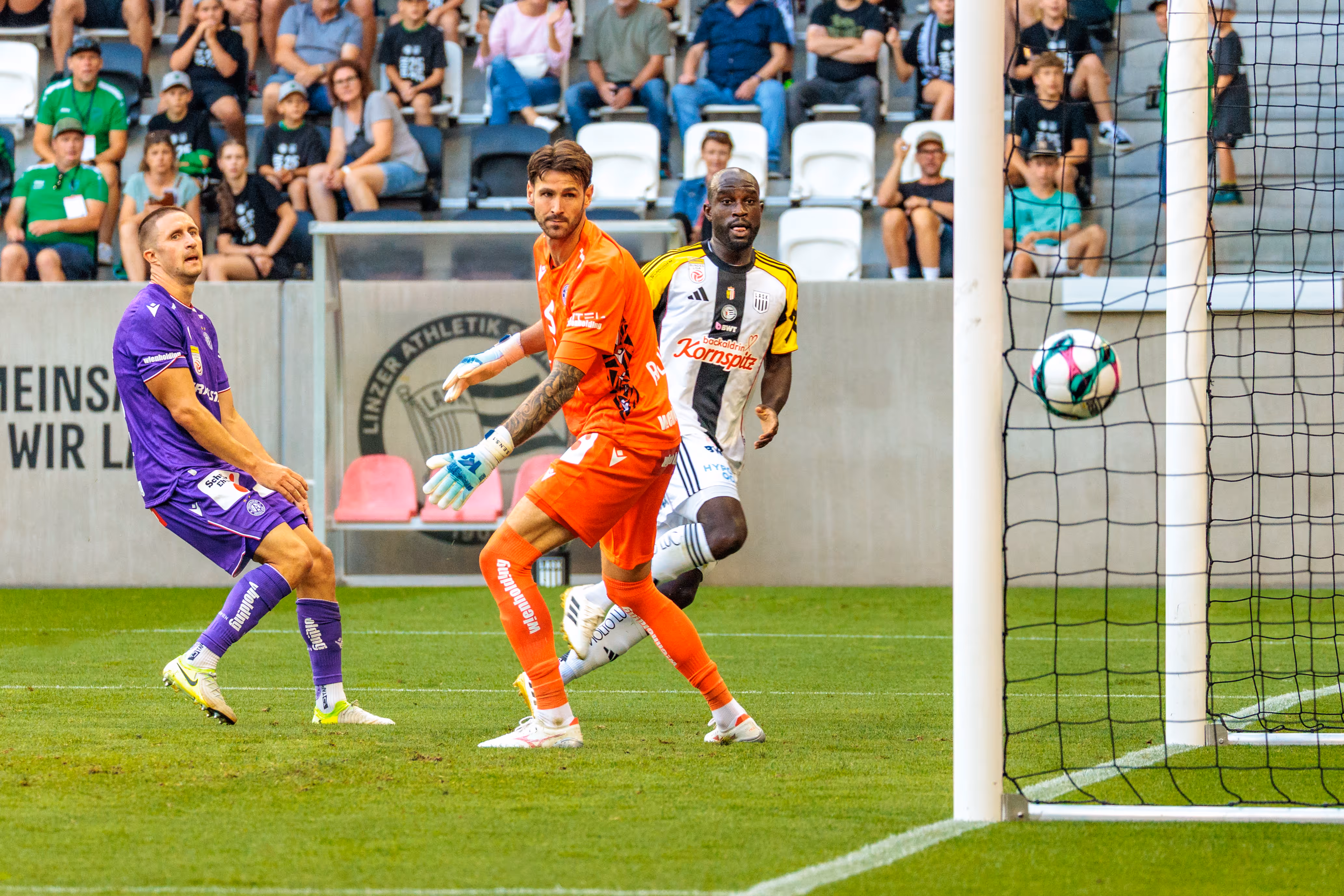 Der Ball liegt im Tornetz, während Fußballspieler des LASK und von Austria Wien auf das soeben erzielte Tor blicken