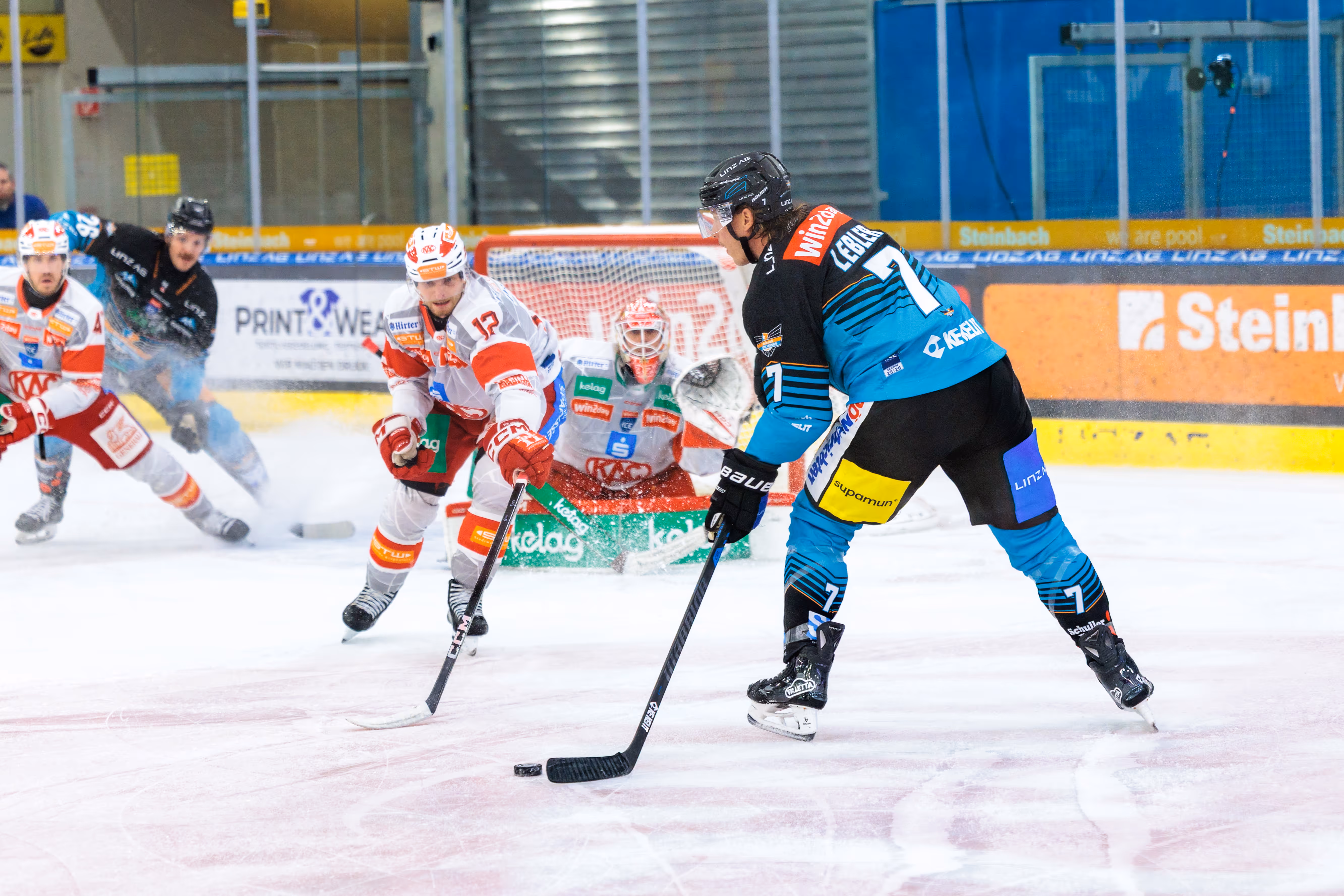 Brian Lebler von den Steinbach Black Wings Linz führt den Puck im Angriff und wird vor dem Tor von einem Spieler des EC-KAC unter Druck gesetzt