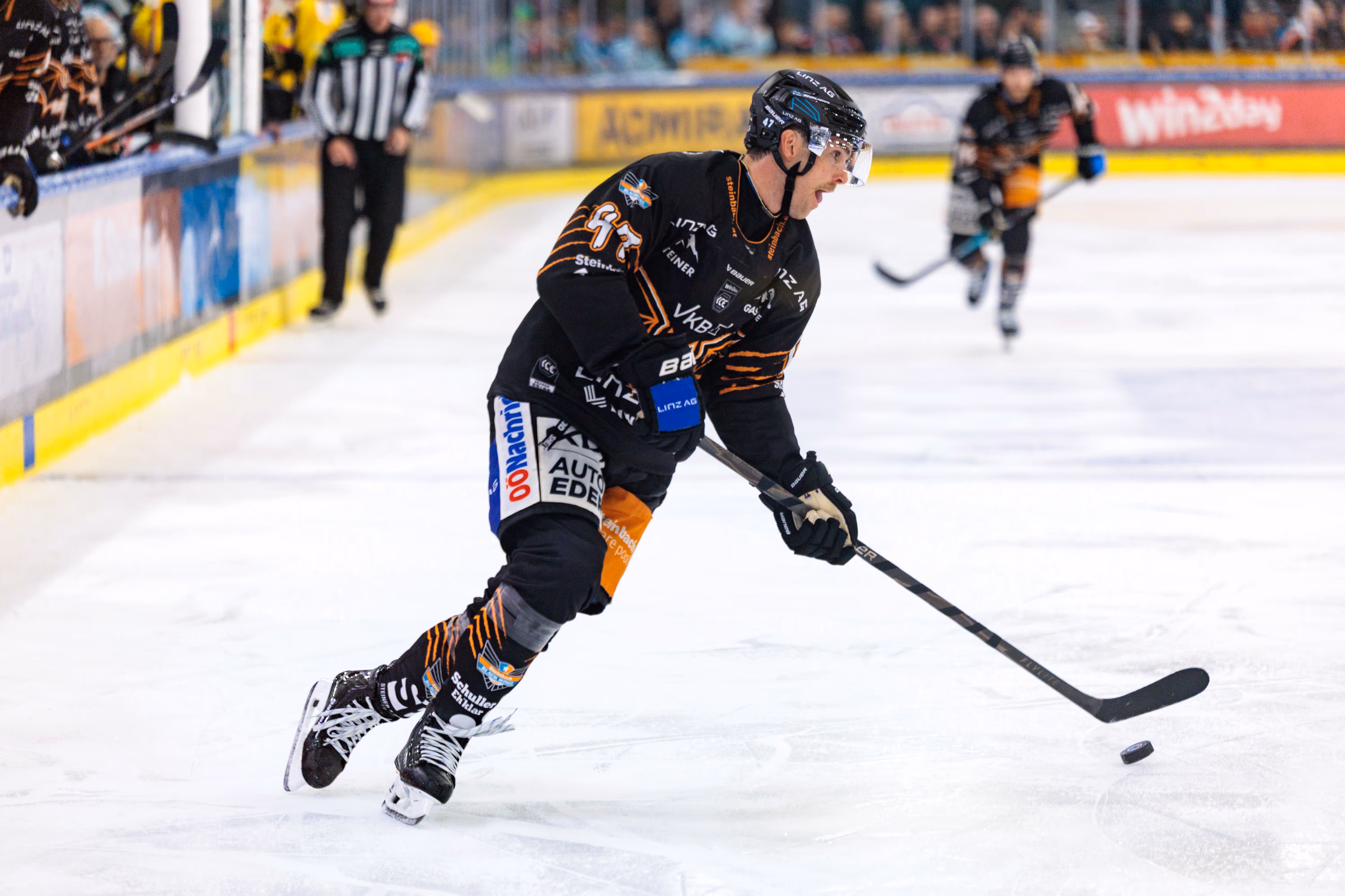 Eishockeyspieler Logan Roe von den Black Wings Linz führt den Puck auf dem Eis während eines Spiels