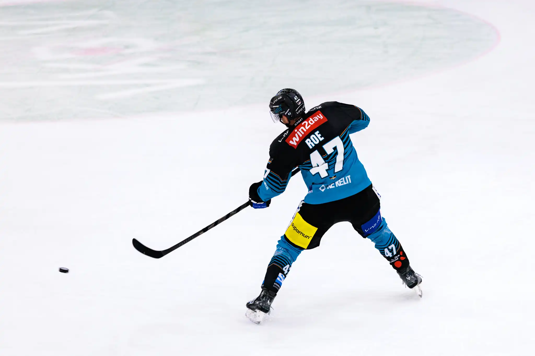 Rückansicht des Eishockeyspielers Logan Roe von den Steinbach Black Wings Linz mit der Nummer 47, der gerade einen kraftvollen Schlagschuss ausführt