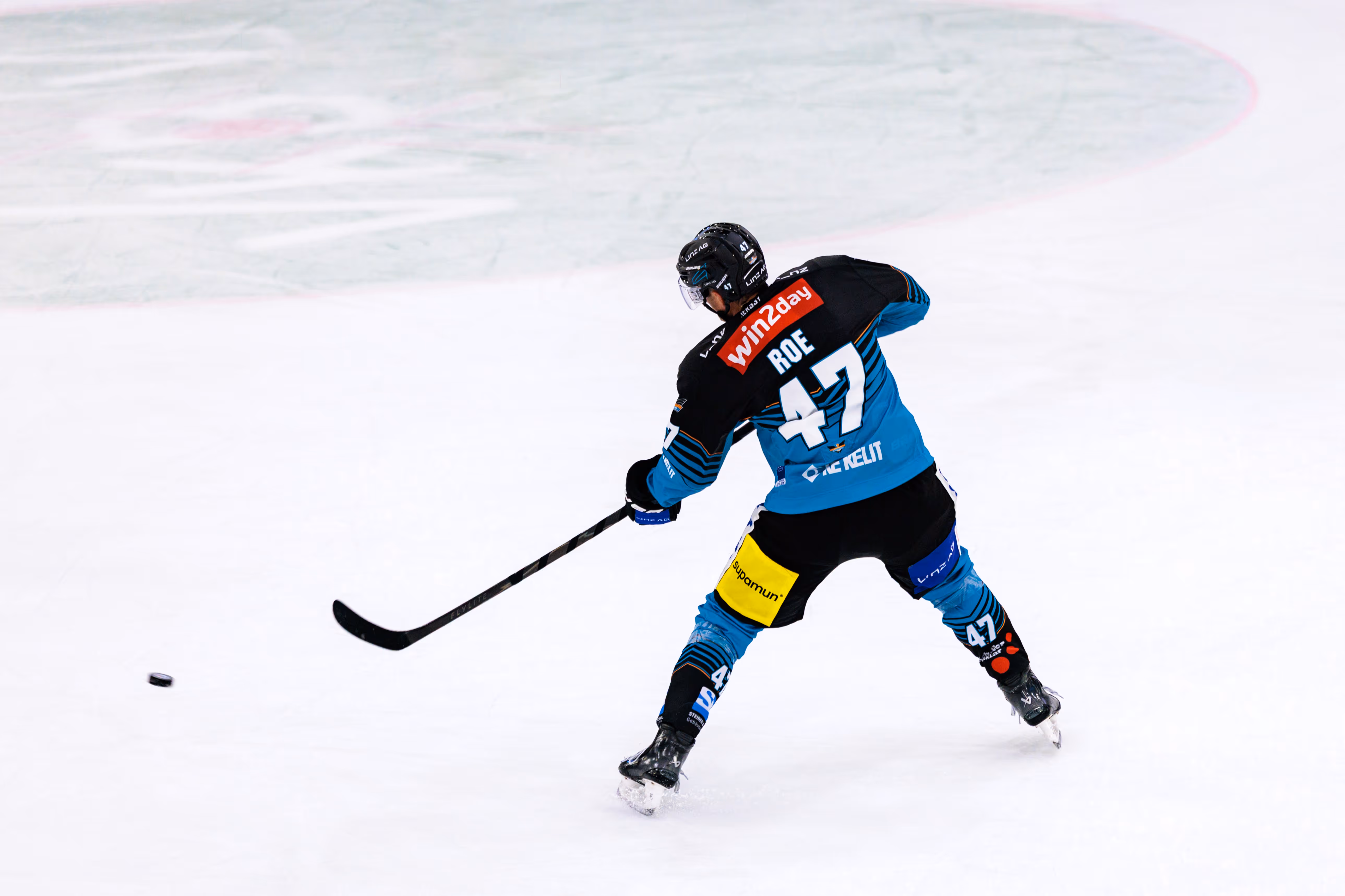Rückansicht des Eishockeyspielers Logan Roe von den Steinbach Black Wings Linz mit der Nummer 47, der gerade einen kraftvollen Schlagschuss ausführt