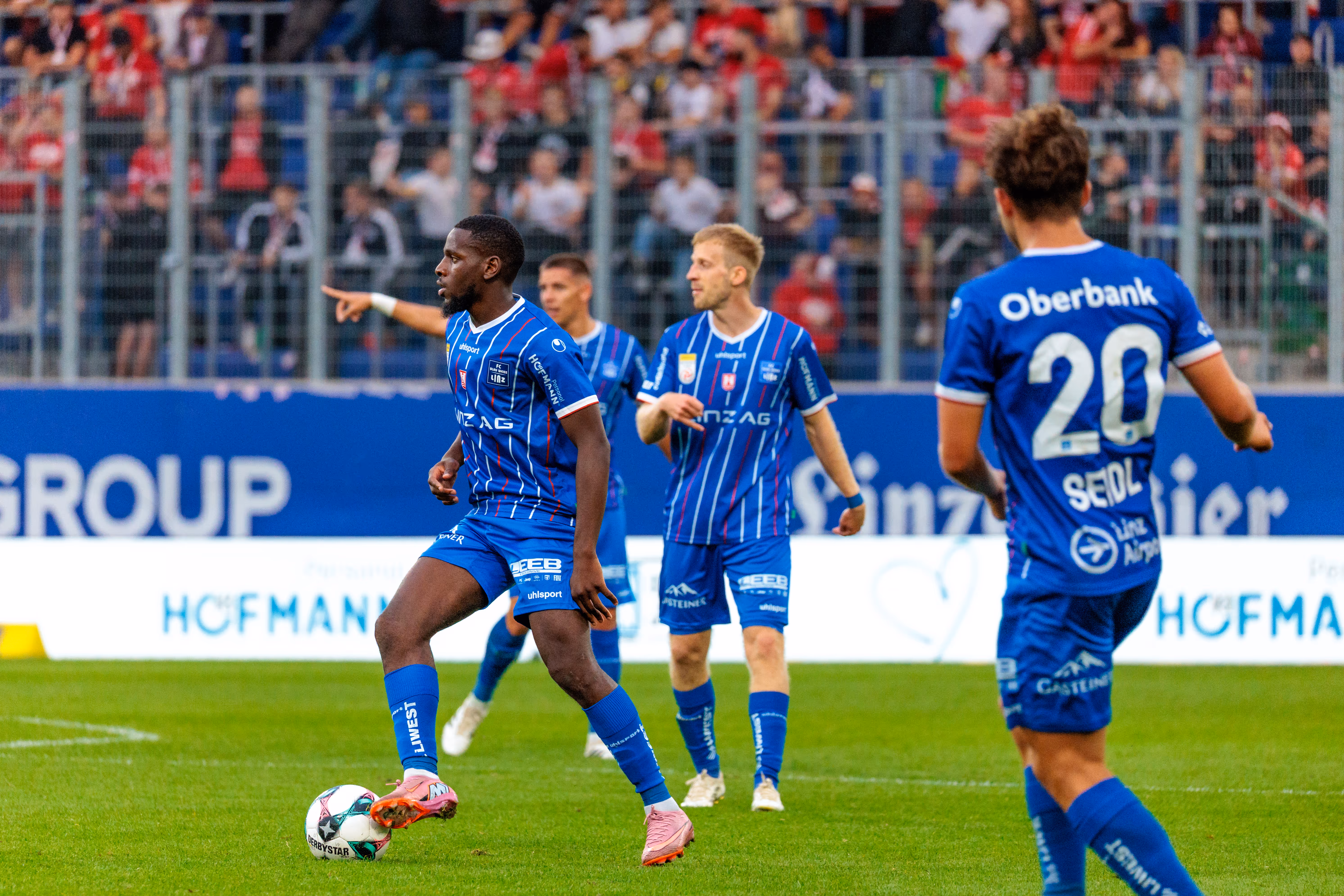 Mamadou Fofana vom FC Blau-Weiß Linz im blau-weiß-rot gestreiften Trikot kontrolliert mit seinen pinken Fußballschuhen den Ball während eines Spielaufbaus im Stadion