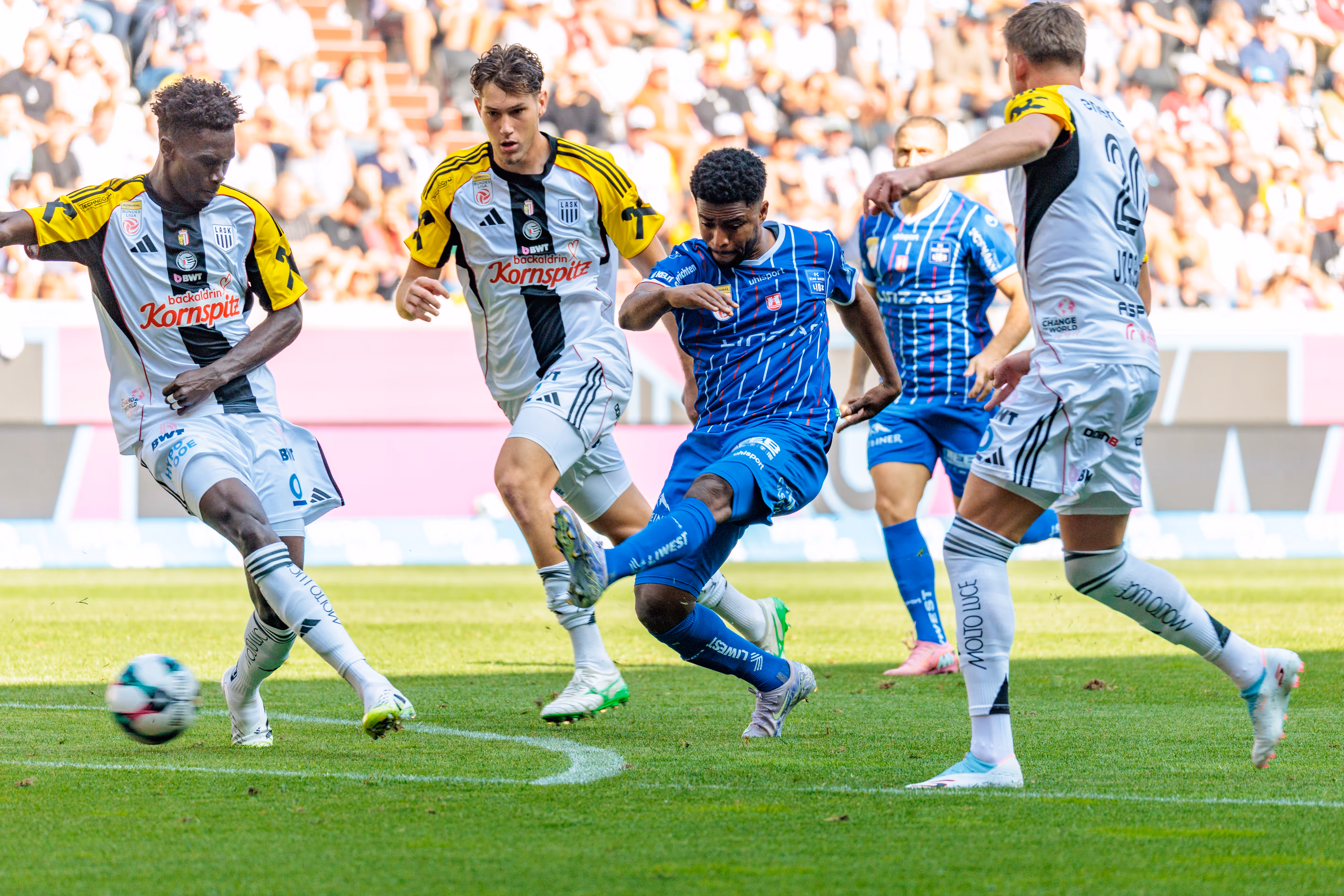 Paul Mensah vom FC Blau-Weiß Linz im Dribbling am Ball, bedrängt von mehreren LASK-Spielern während des Linzer Derbys