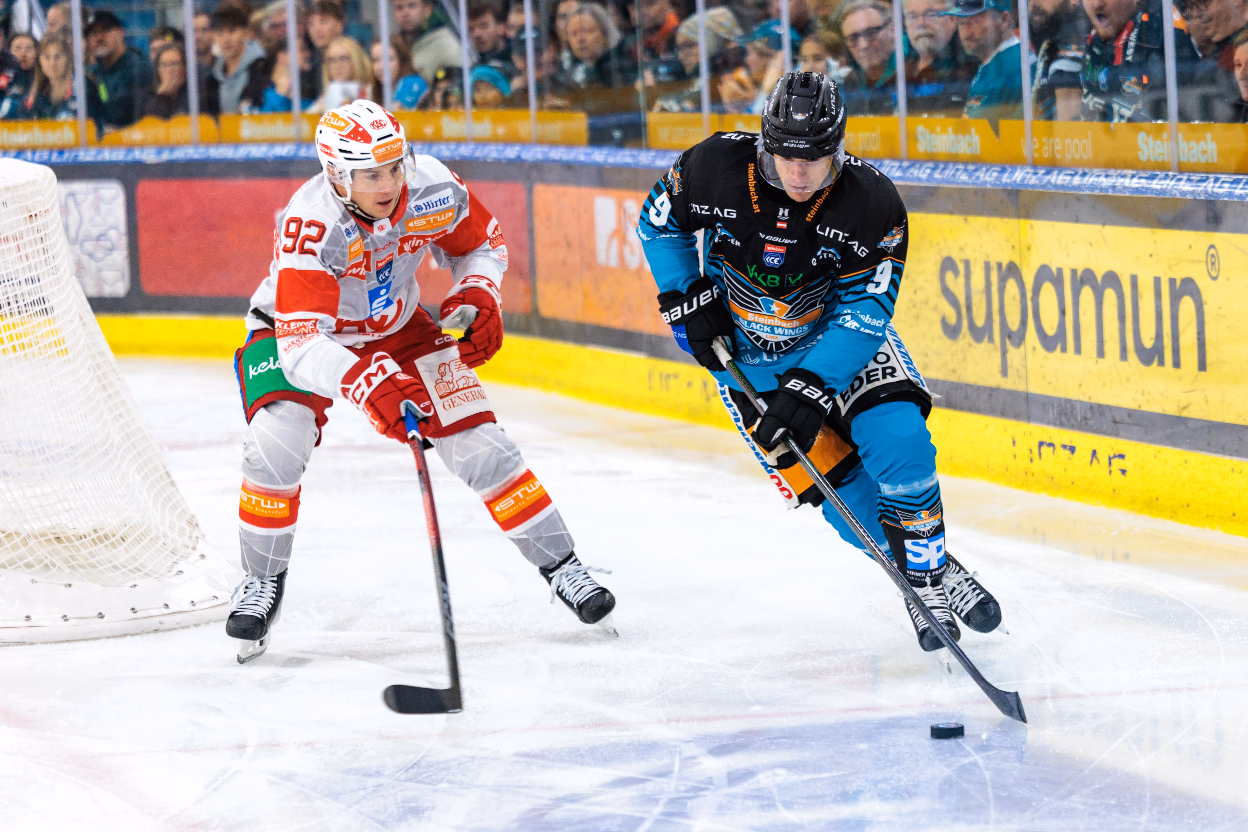 Der Eishockeyspieler Greg Moro von den Black Wings Linz führt den Puck und wird dabei von Clemens Unterweger vom EC-KAC vor dem Tor verteidigt