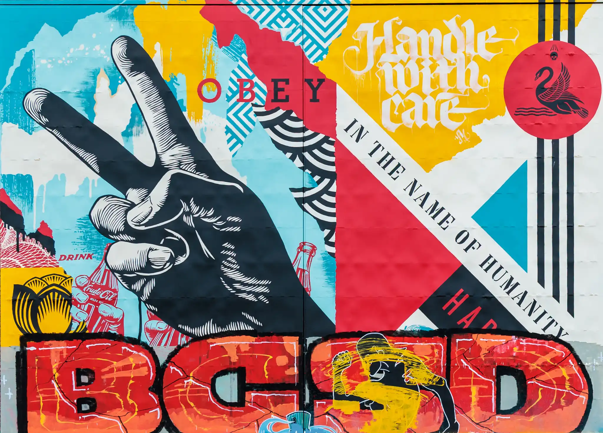 Ein vielseitiges Pop-Art-Wandgemälde zeigt eine Hand, die das Friedenszeichen formt, umgeben von den Botschaften 'OBEY' und 'Handle with care', abstrakten Mustern und einem Emblem mit Schwan und Totenkopf