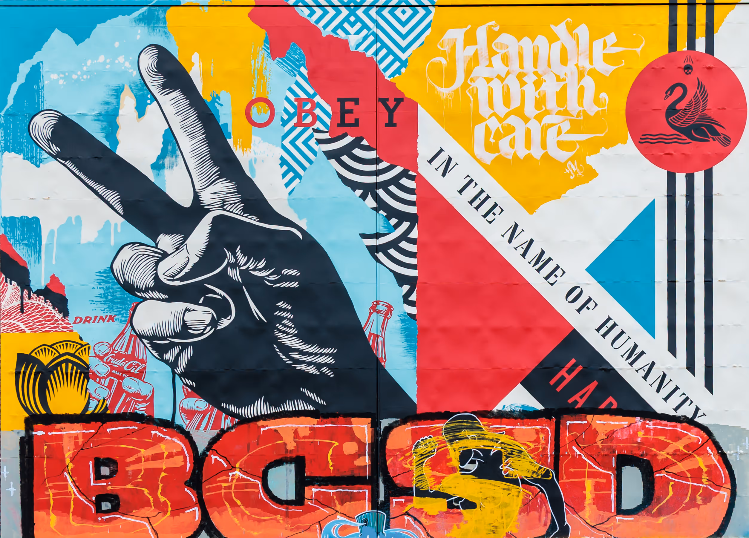 Ein vielseitiges Pop-Art-Wandgemälde zeigt eine Hand, die das Friedenszeichen formt, umgeben von den Botschaften 'OBEY' und 'Handle with care', abstrakten Mustern und einem Emblem mit Schwan und Totenkopf 