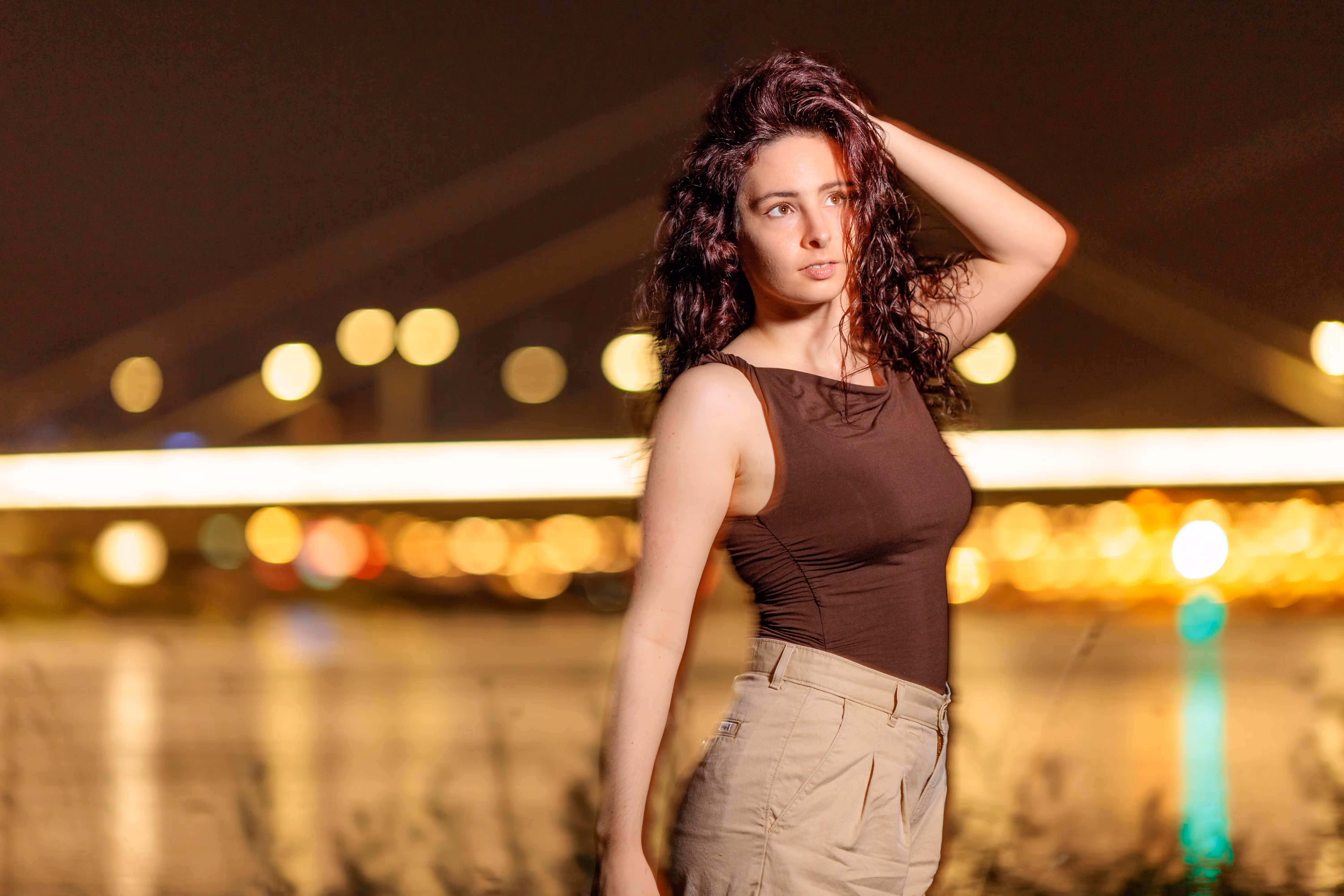 Ein atmosphärisches Nachtporträt von Nicole mit lockigem Haar, die vor einem unscharfen Hintergrund aus goldenen Stadtlichtern in Linz posiert