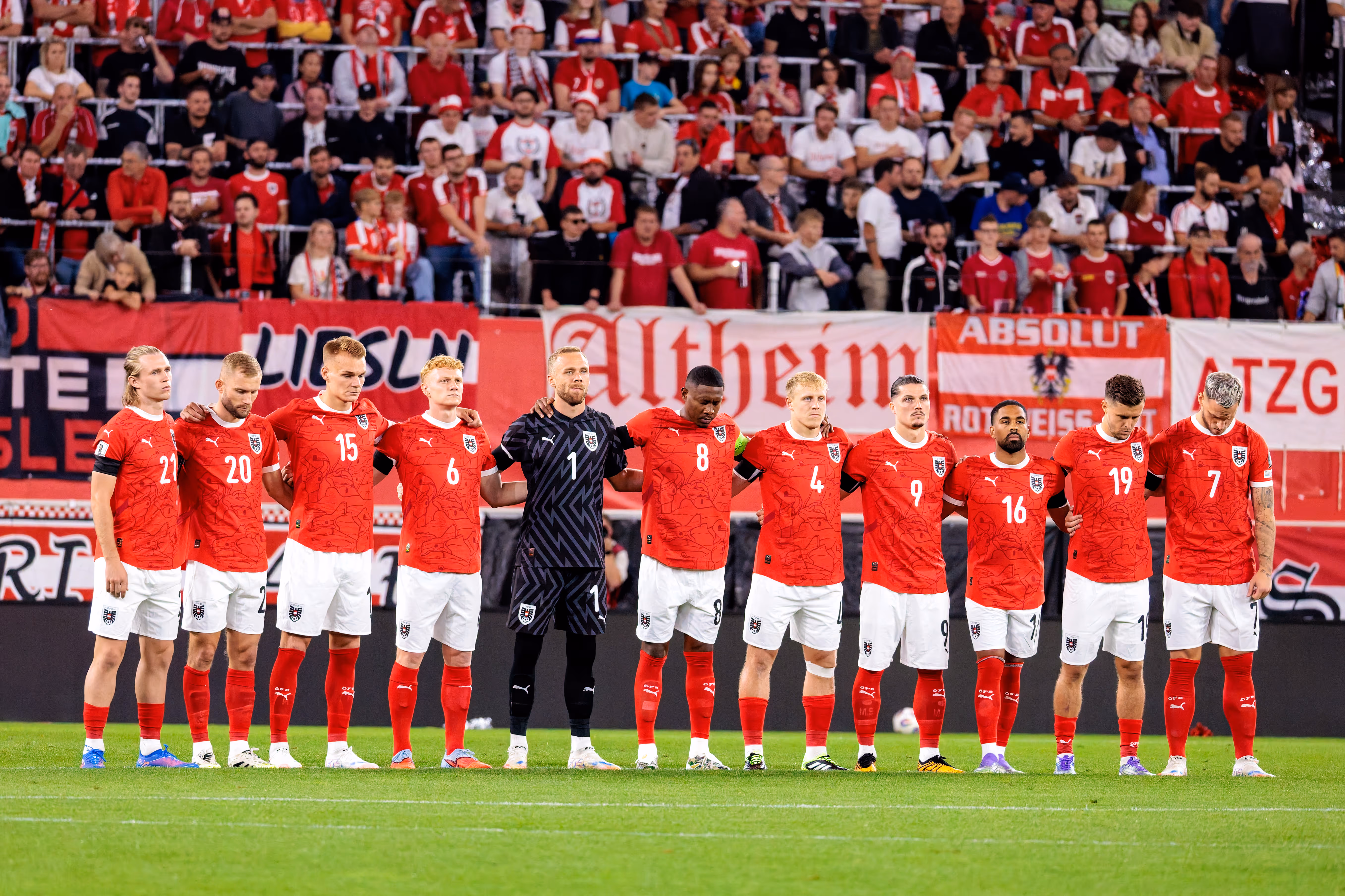 Die österreichische Fußballnationalmannschaft steht in roten Trikots eng zusammen auf dem Spielfeld und hält eine Schweigeminute ab