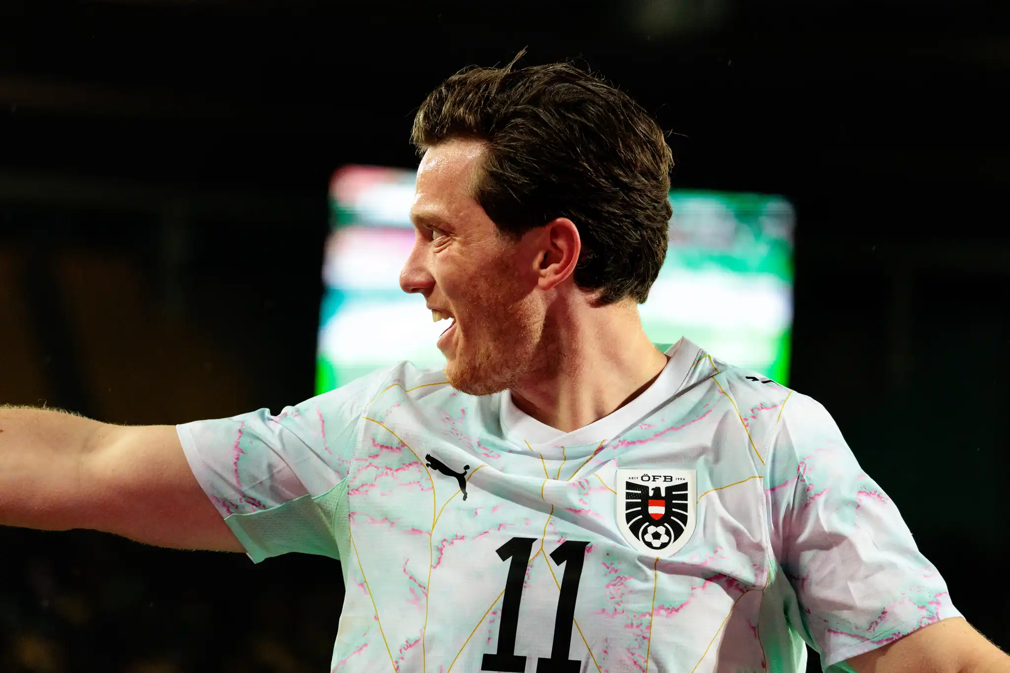 Ein österreichischer Fußballspieler im Trikot mit der Nummer 11 jubelt strahlend mit offenem Mund und Blick zur Seite