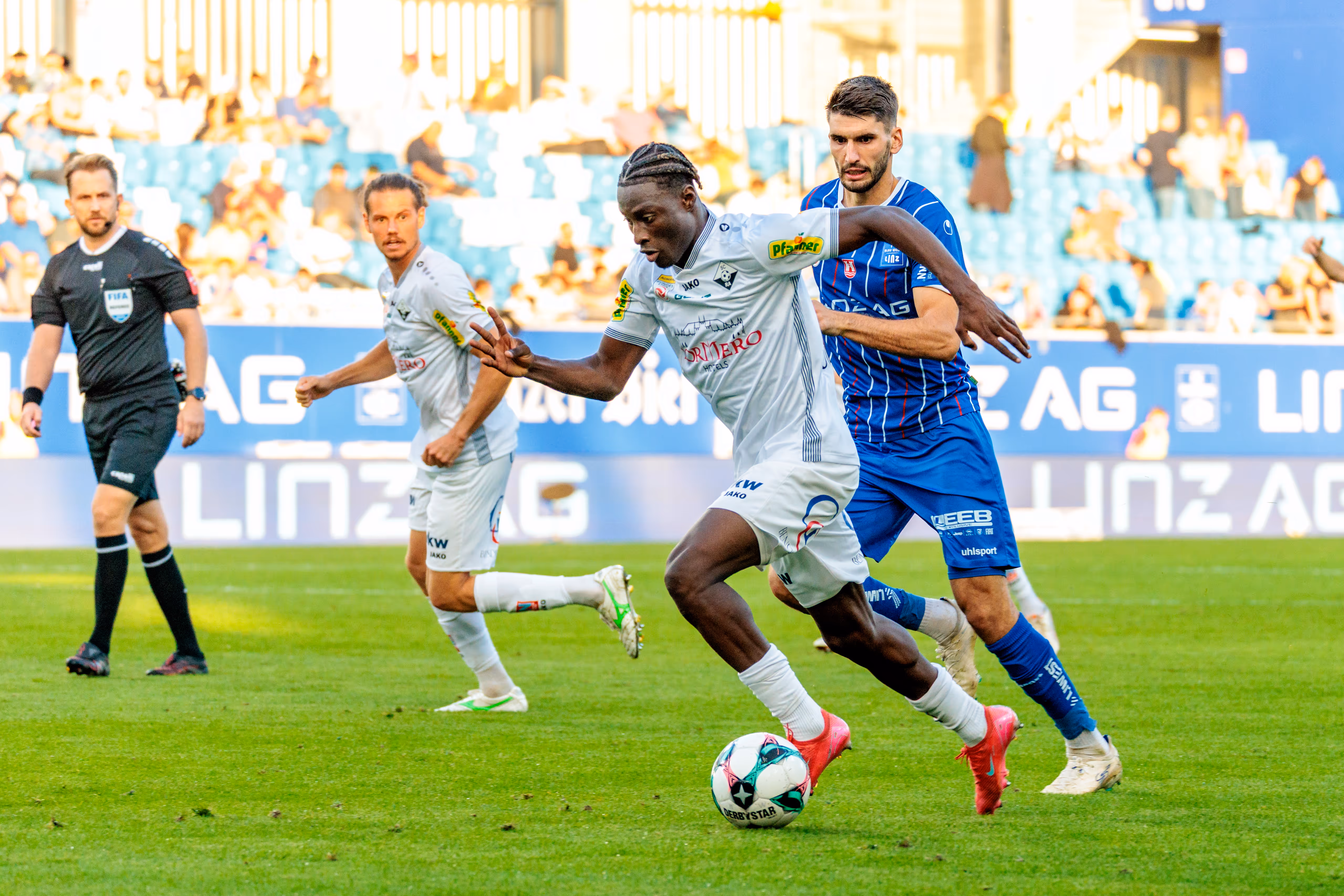 Der Altacher Spieler Ousmane Diawara in einem dynamischen Dribbling mit dem Ball, dicht verfolgt von einem Gegenspieler des FC Blau-Weiß Linz
