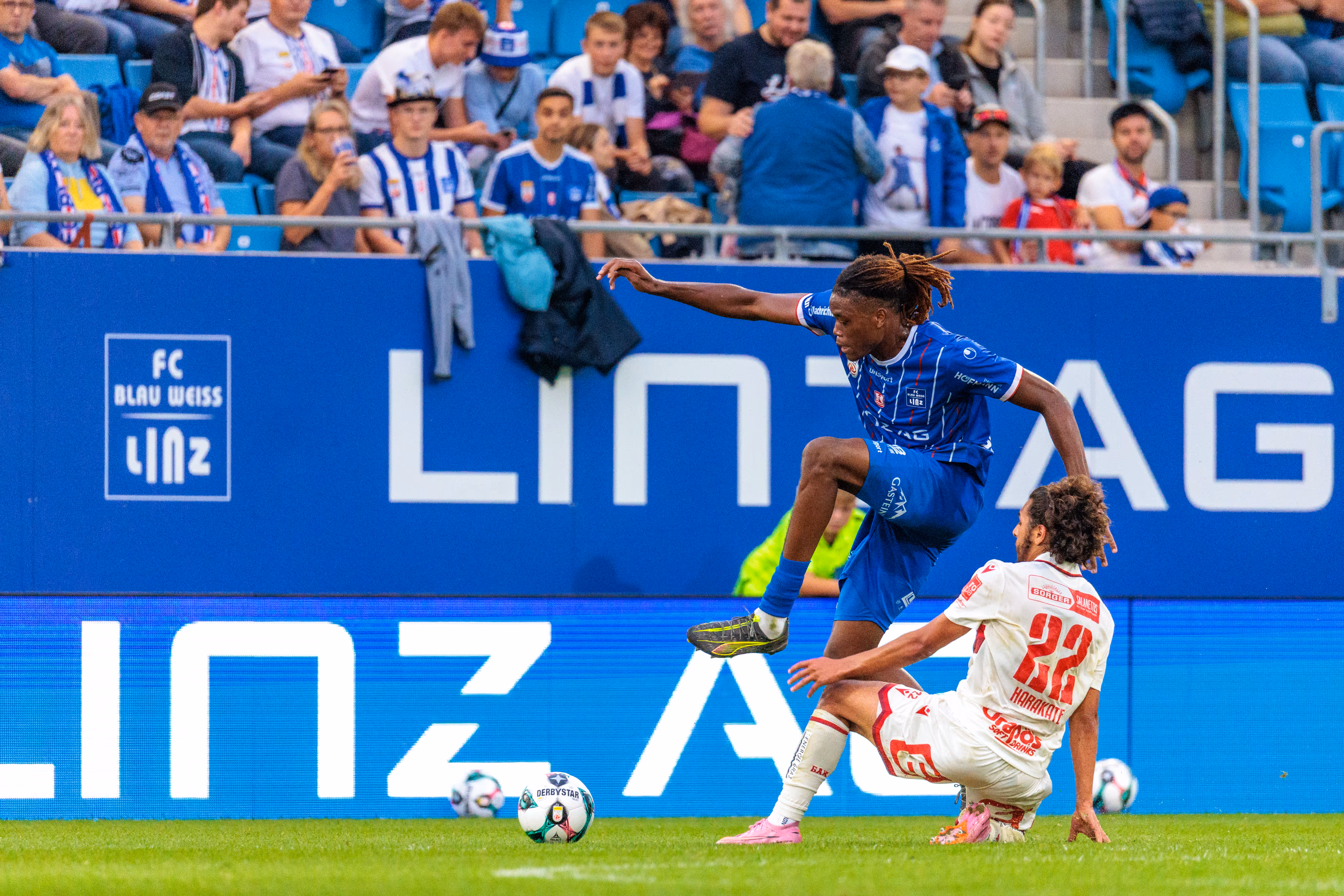 Alem Pasic vom FC Blau-Weiß Linz überspringt in einem dynamischen Zweikampf die Grätsche des am Boden liegenden GAK-Spielers Ramiz Harakate