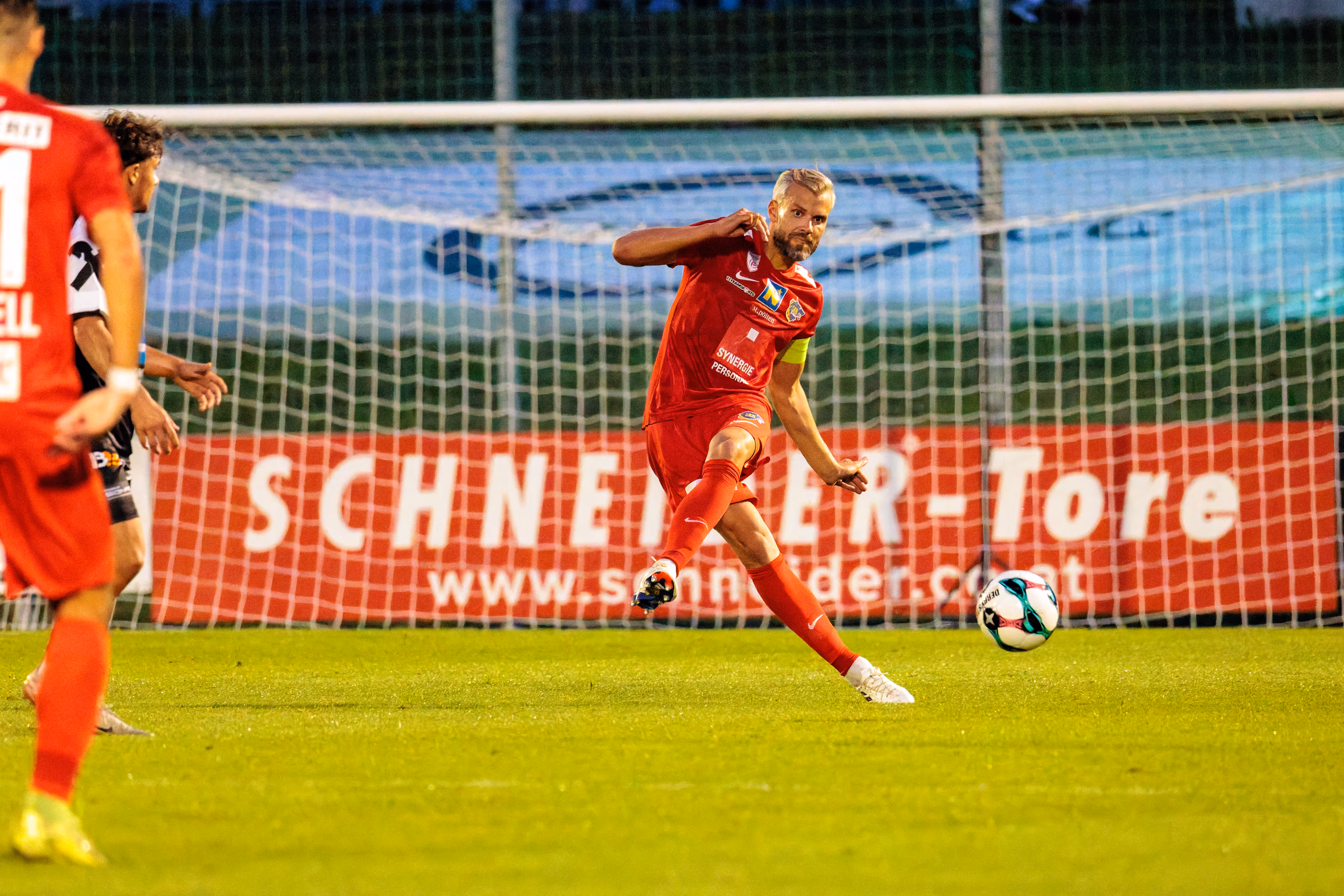 Ein Spieler des SKN St. Pölten im roten Trikot mit Kapitänsbinde spielt während eines ÖFB-Cup-Spiels einen präzisen Pass nach vorne