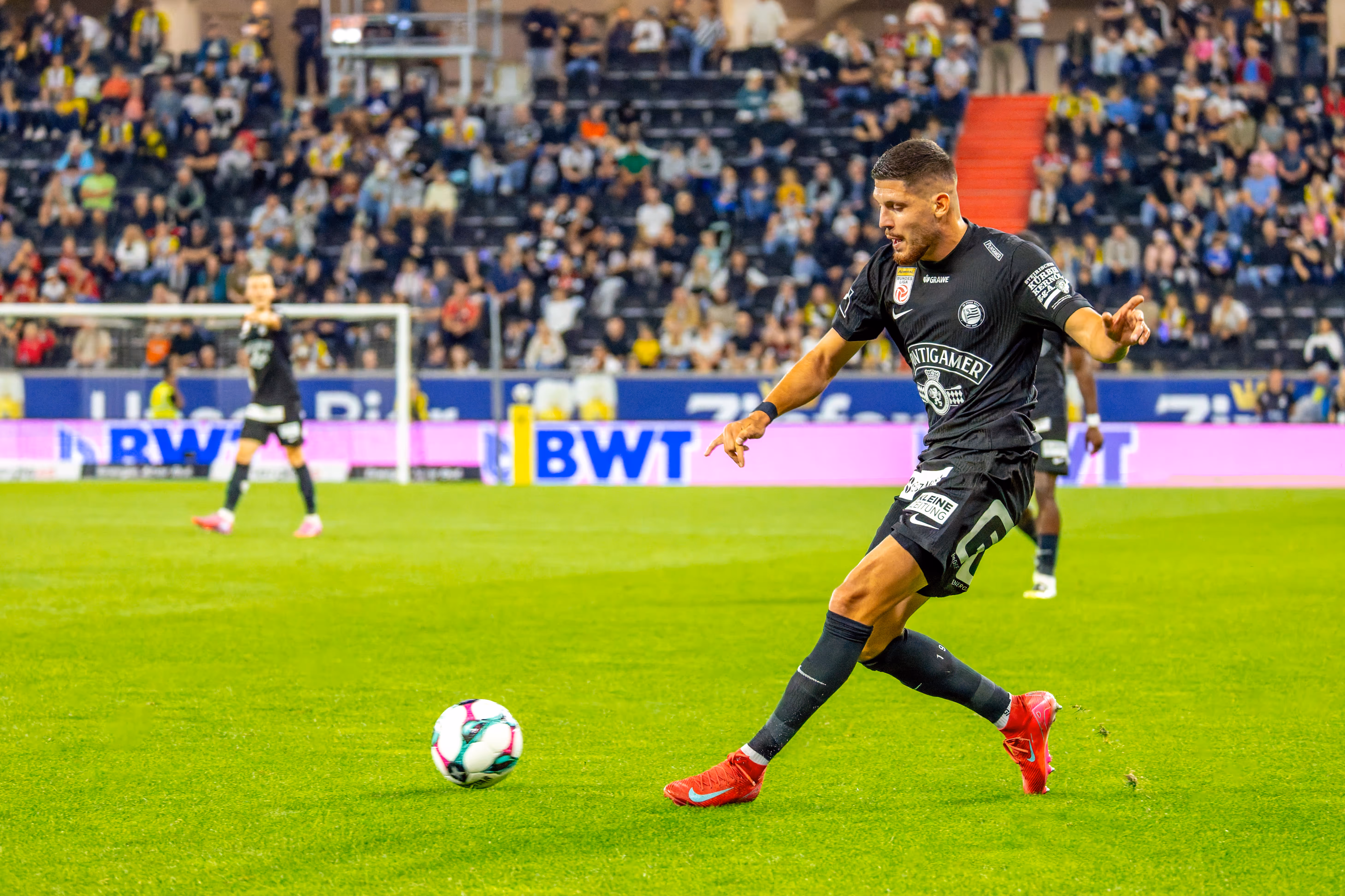Ein Fußballspieler des SK Sturm Graz in schwarzem Trikot passt den Ball bei einem Bundesligaspiel in der Raiffeisen Arena