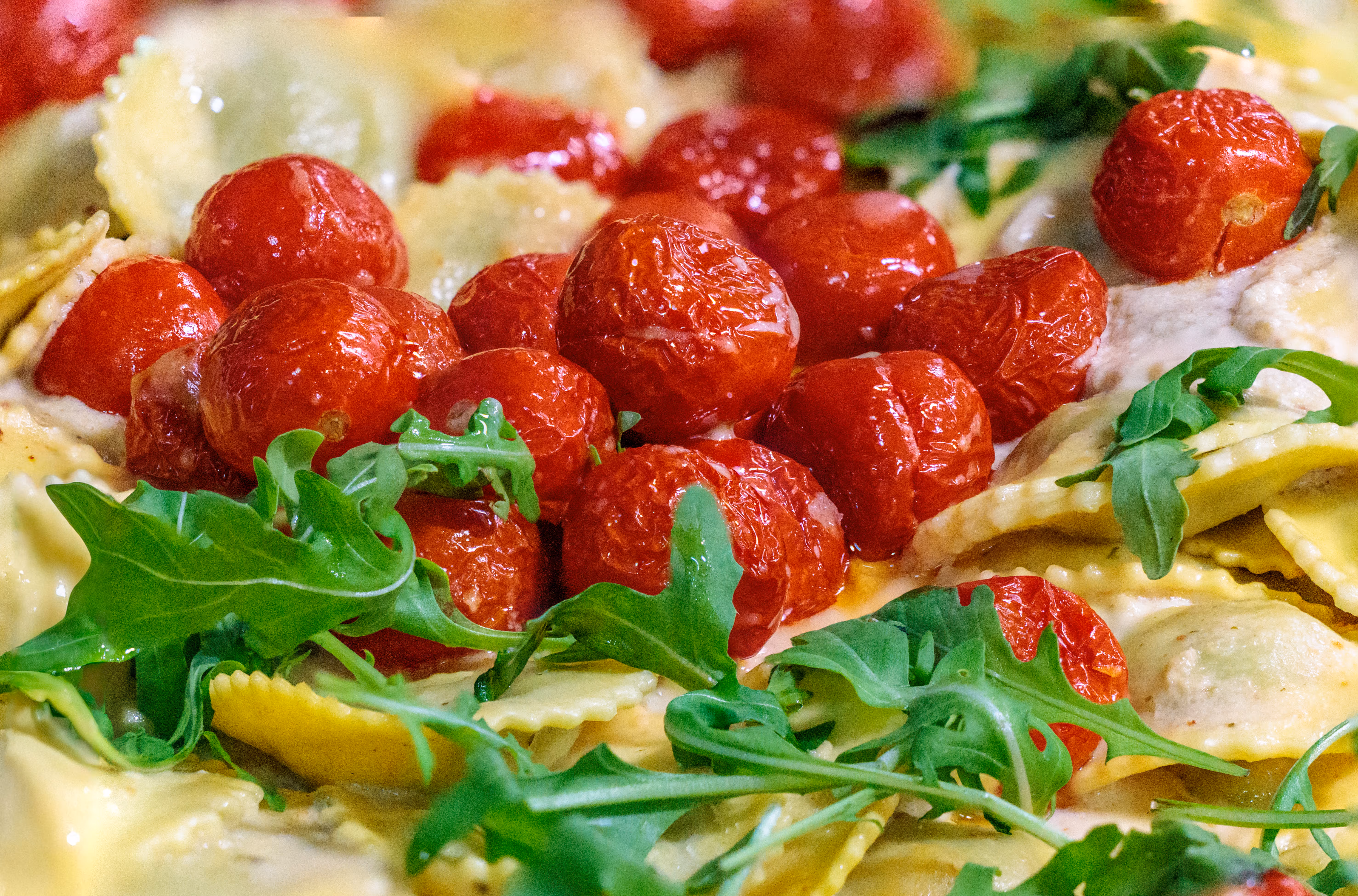 Nahaufnahme eines Pastagerichts mit frischen Ravioli in einer cremigen Soße, garniert mit gerösteten Kirschtomaten und Rucola