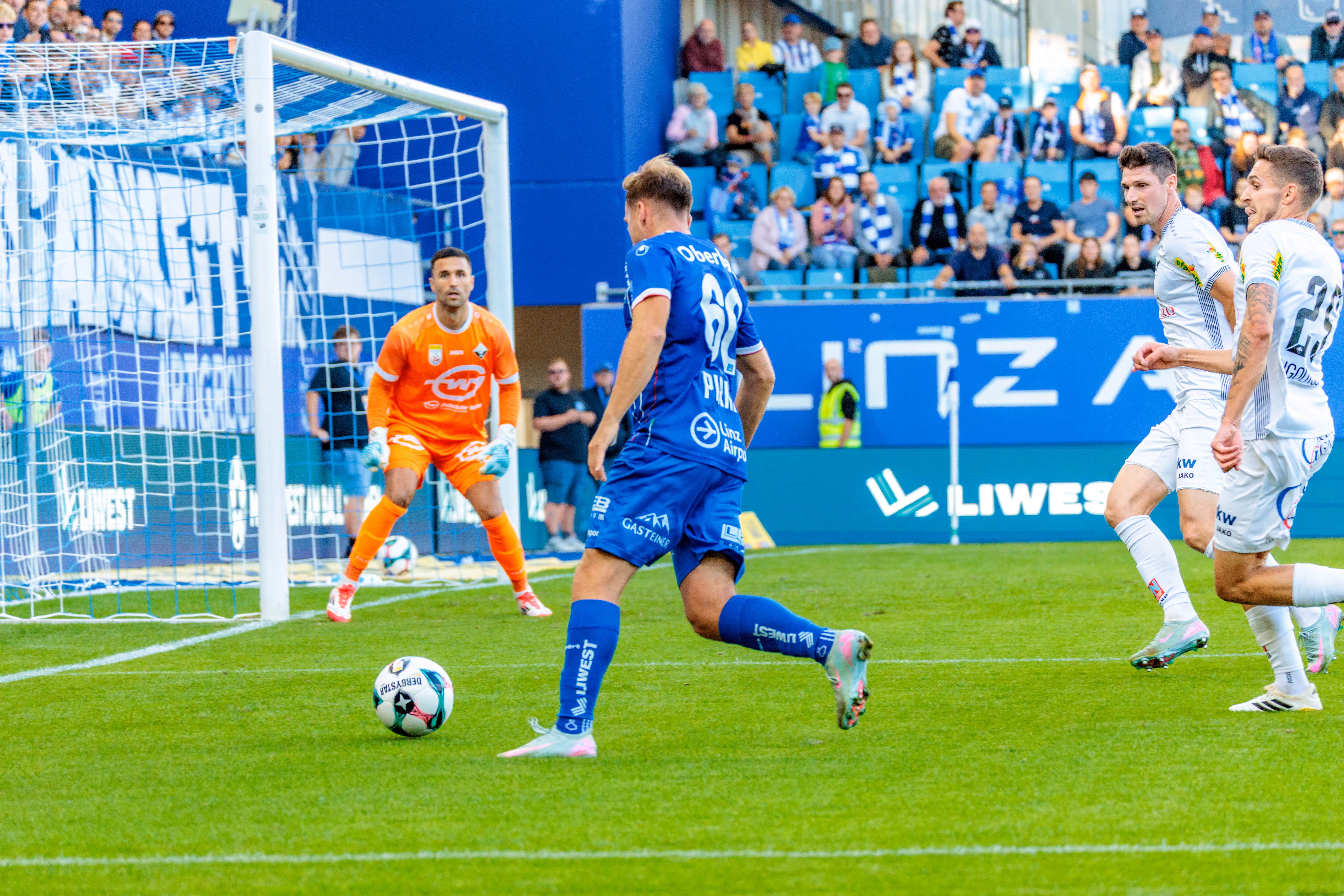 Der Fußballspieler Paul Mensah vom FC Blau-Weiß Linz schießt den Ball in Richtung des Tores, das von Altach-Tormann Dejan Stojanovic in Orange verteidigt wird