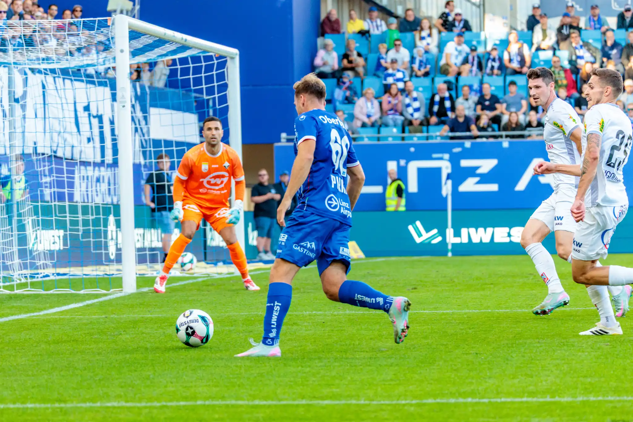 Der Fußballspieler Paul Mensah vom FC Blau-Weiß Linz schießt den Ball in Richtung des Tores, das von Altach-Tormann Dejan Stojanovic in Orange verteidigt wird
