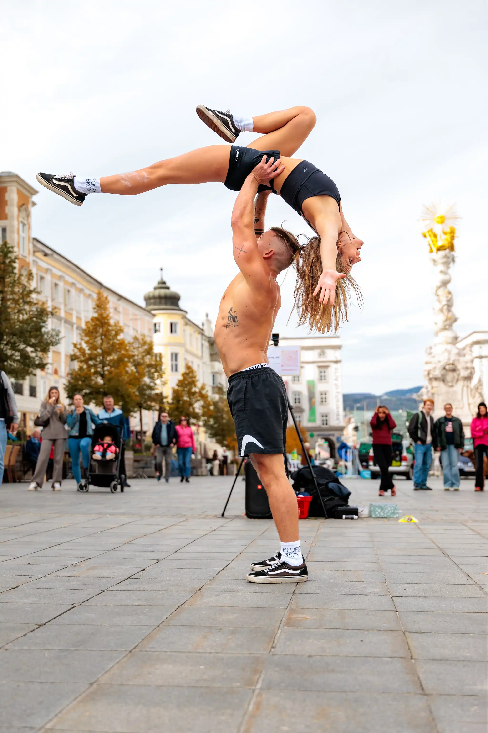 Zwei Akrobaten führen eine beeindruckende Hebefigur auf einem belebten Stadtplatz vor Publikum auf