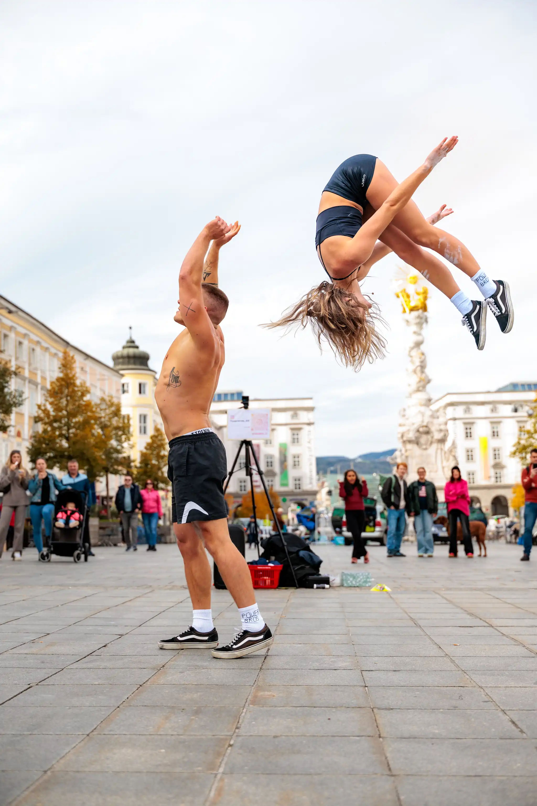 Zwei Akrobaten der Power Bros führen auf einem städtischen Hauptplatz eine beeindruckende Turnübung mit einem Salto rückwärts durch