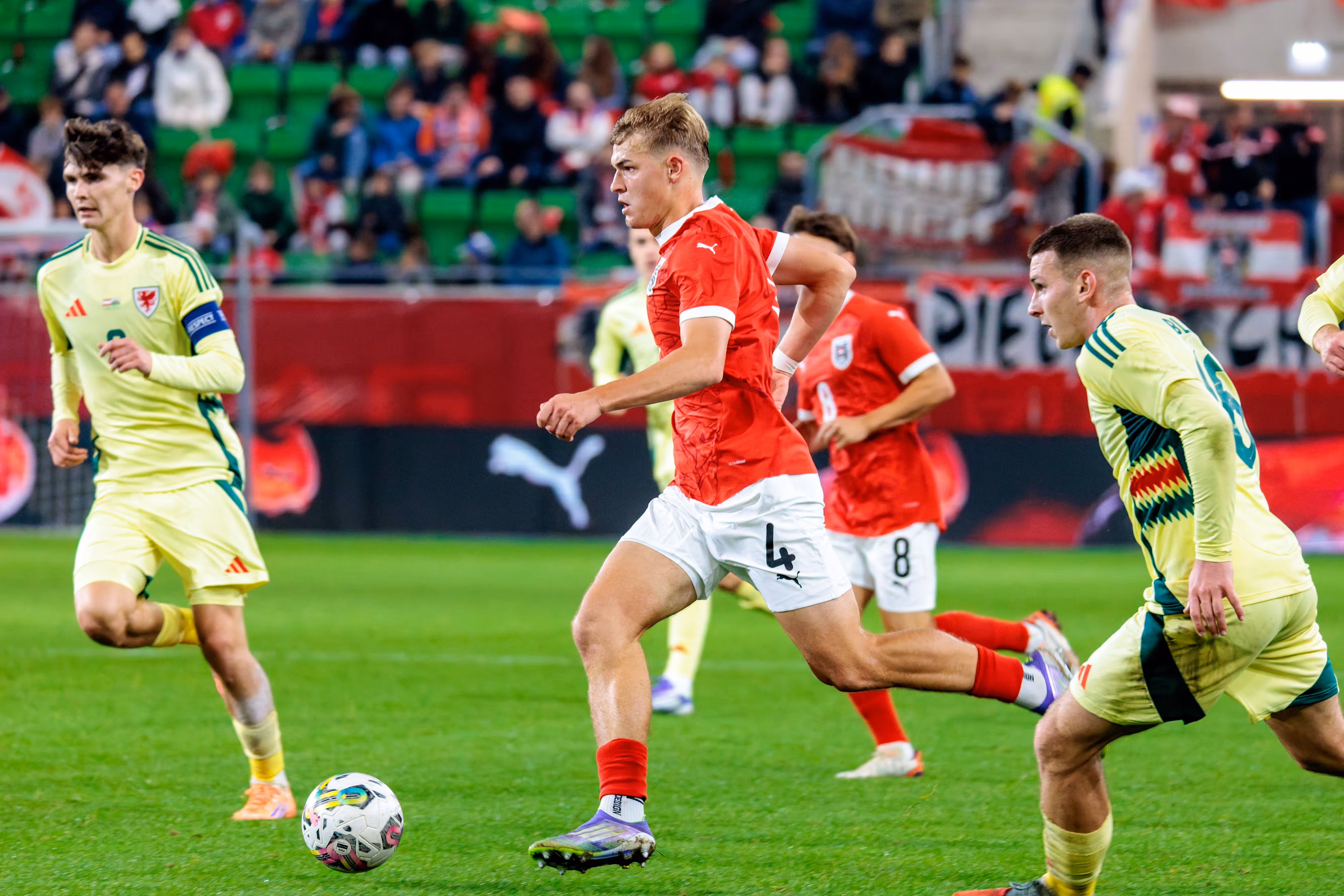 Der österreichische U21-Nationalspieler David Piczka sprintet im roten Trikot mit dem Ball am Fuß, während er von einem walisischen Gegenspieler verfolgt wird