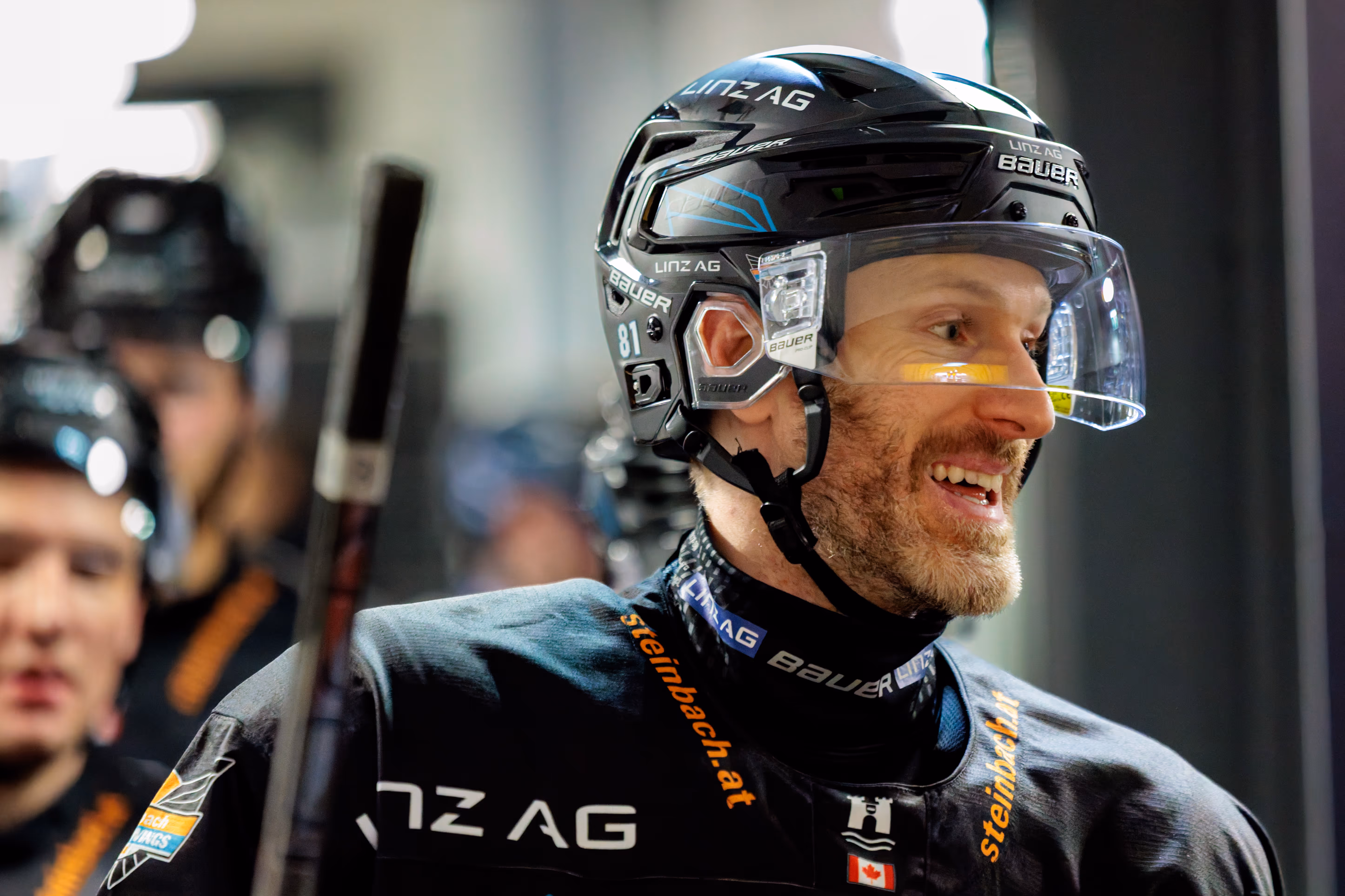 Nahaufnahme des lächelnden Eishockeyspielers Sean Collins von den Steinbach Black Wings Linz in seiner schwarzen Ausrüstung mit Helm