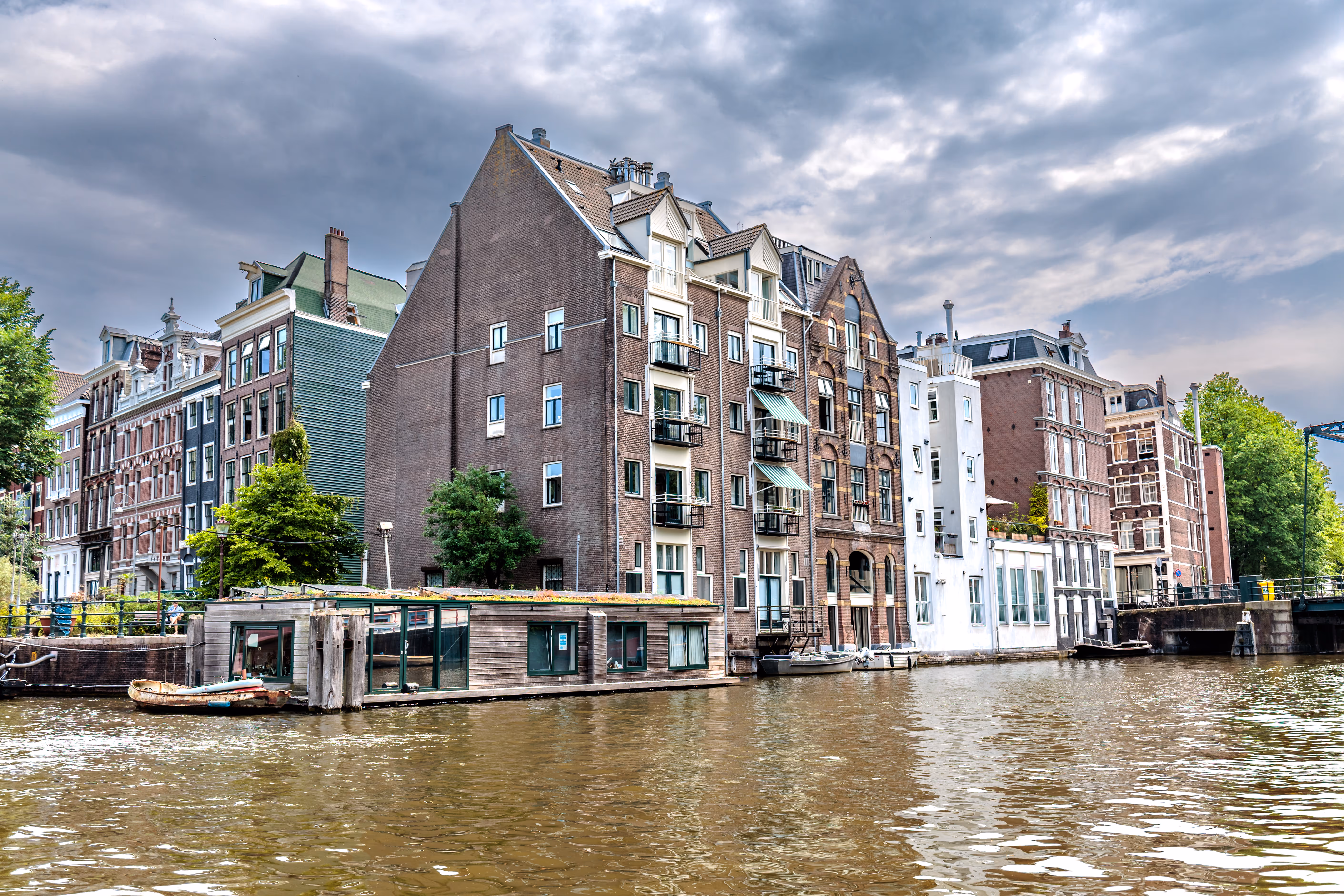 Ein Amsterdamer Kanal gesäumt von schmalen Backsteinhäusern und Hausbooten unter einem bedeckten Himmel 