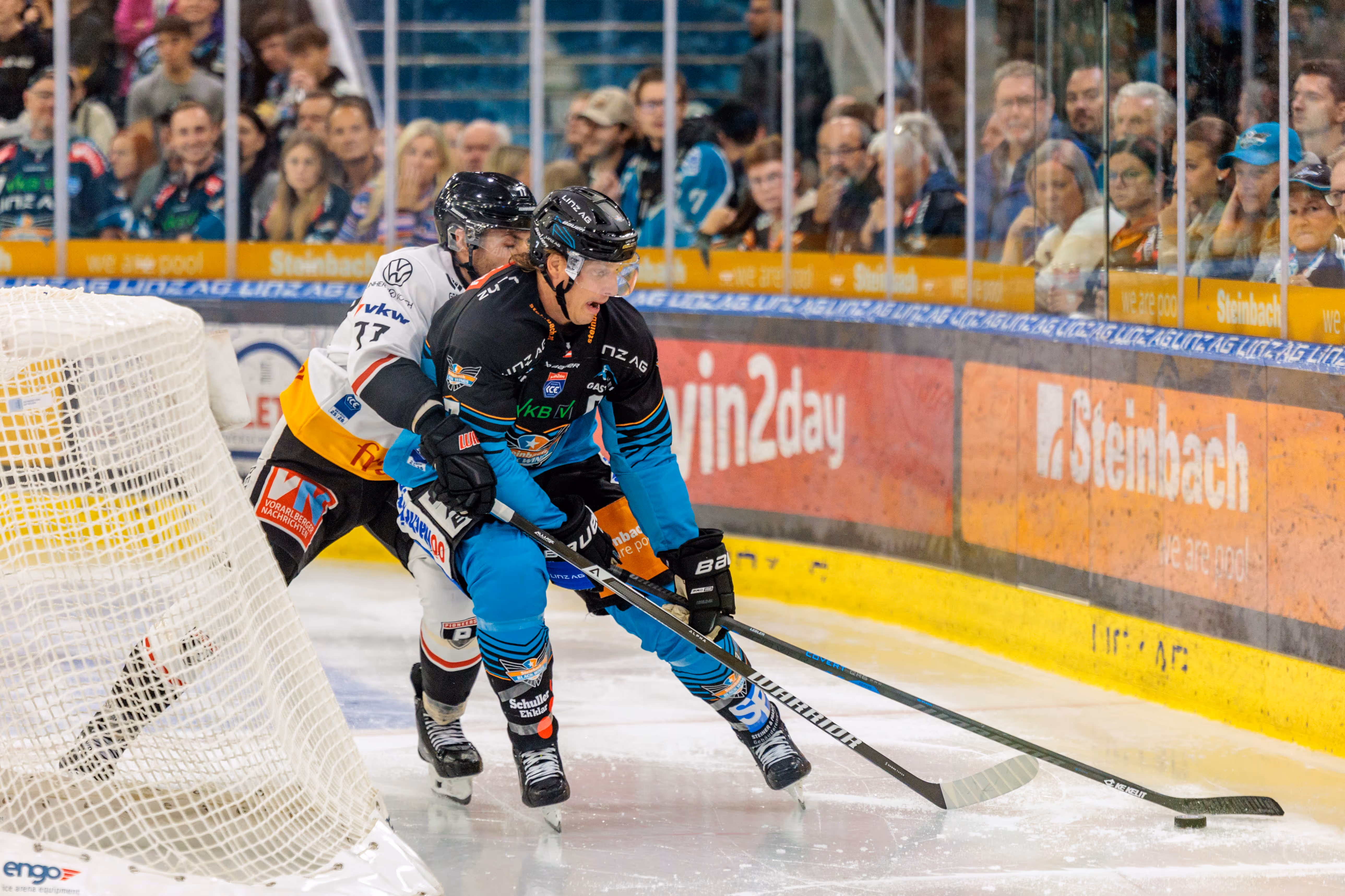 Eishockeyspieler Emilio Romig der Black Wings Linz kämpft mit einem Gegenspieler der Pioneers Vorarlberg vor dem Tor um den Puck