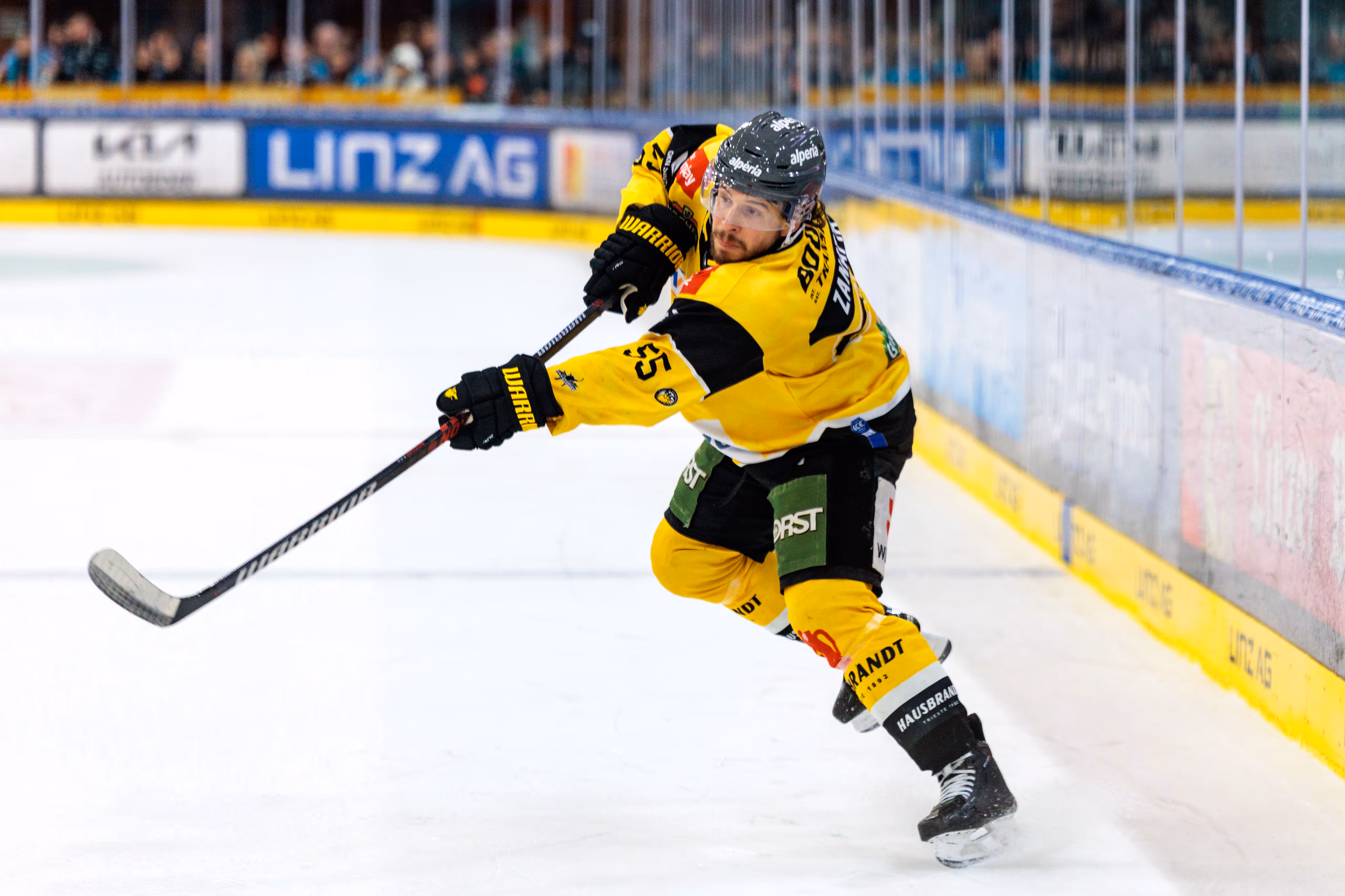 Austin Rueschhoff vom HC Pustertal in seinem gelb-schwarzen Trikot bei einem kraftvollen Schuss während des Eishockeyspiels