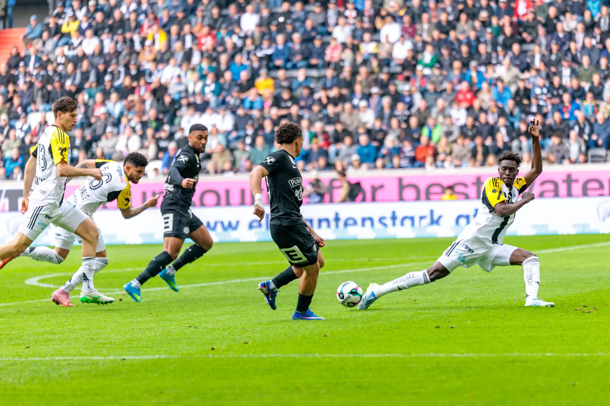 Ein LASK-Spieler streckt sein Bein nach hinten aus um den Pass eines Sturm-Graz-Angreifers zu blockieren