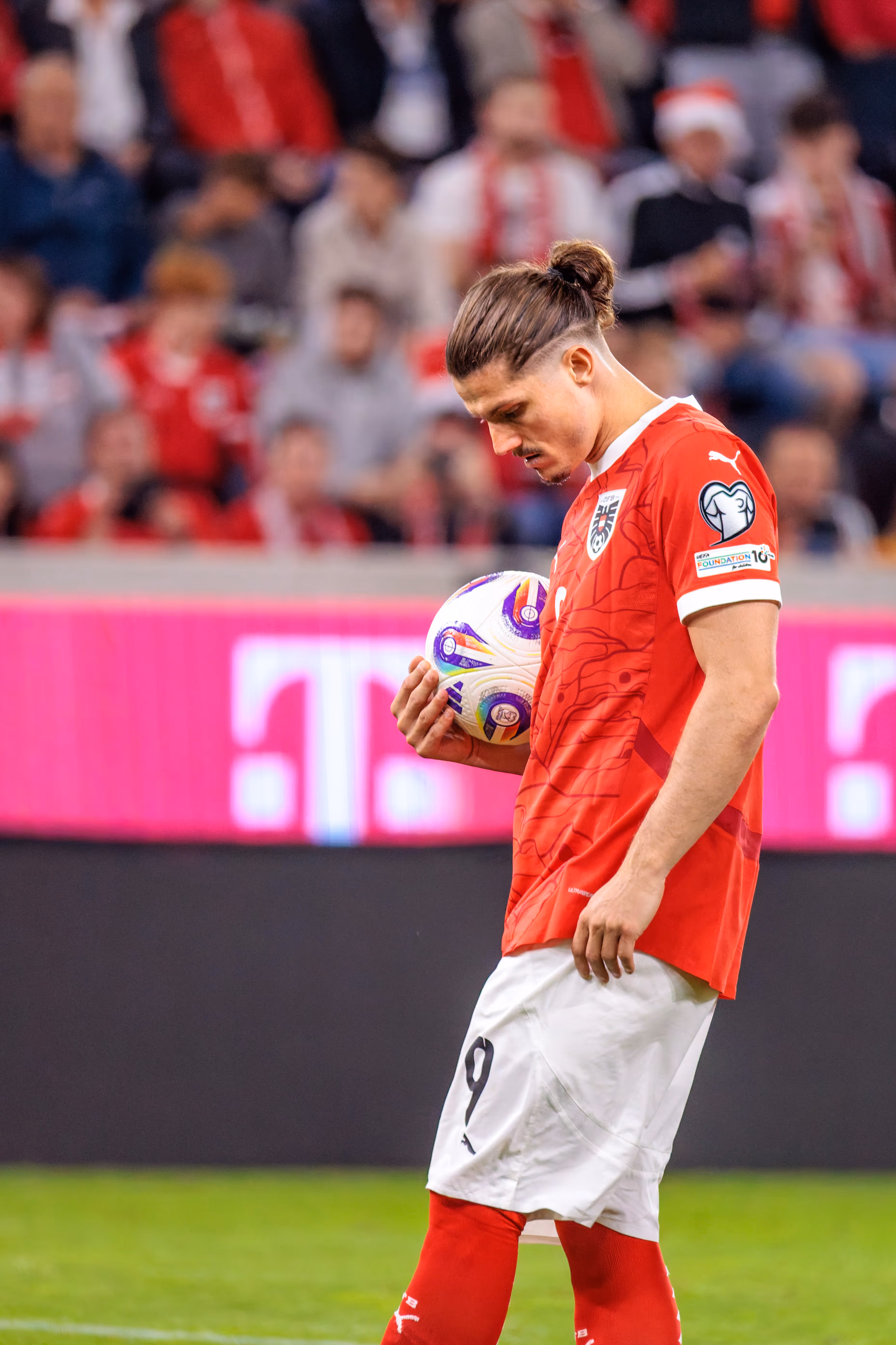 Fußballspieler Marcel Sabitzer in seinem roten Trikot mit der Nummer 9 hält nachdenklich den Fußball, bevor er zum Elfmeter antritt