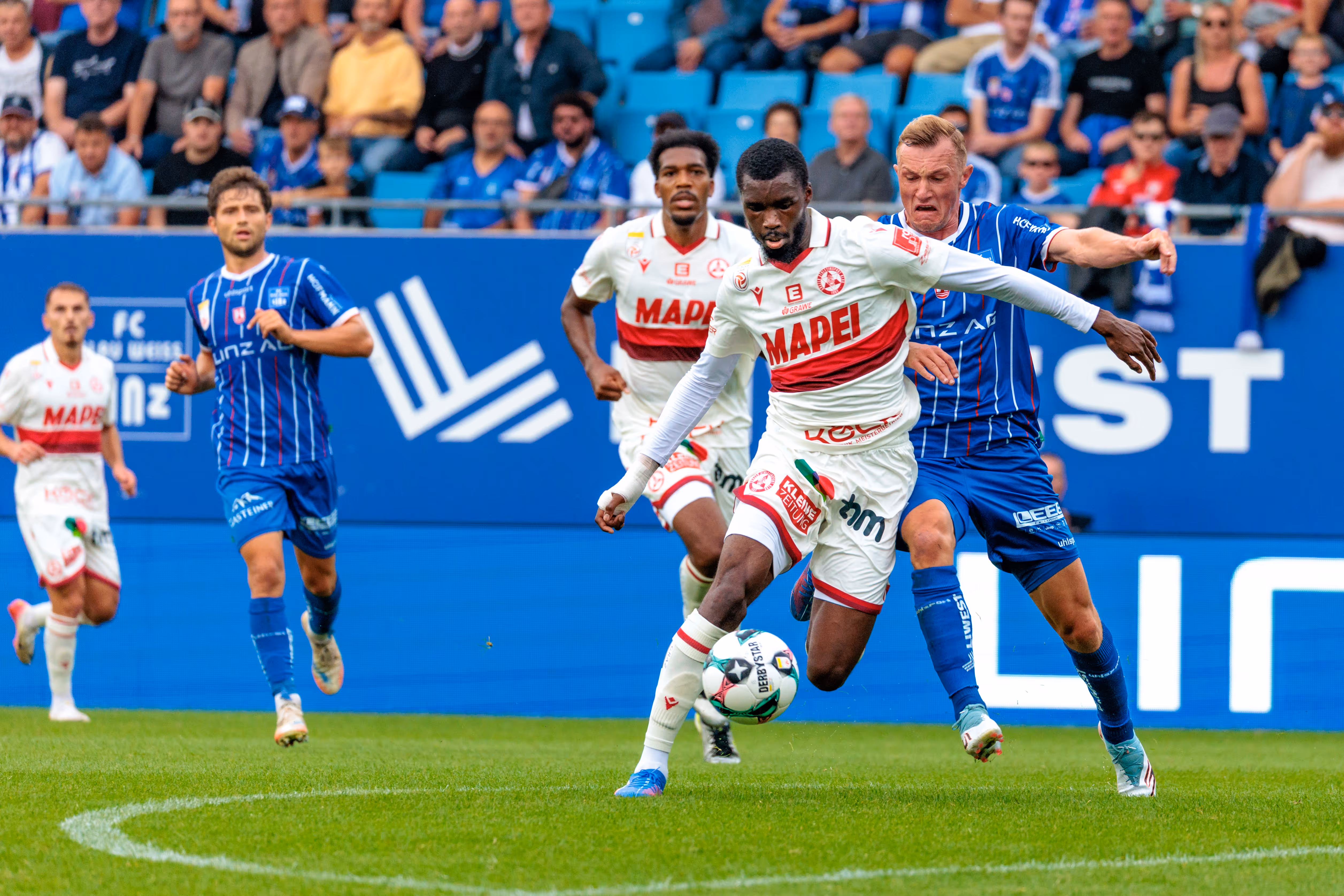 Sadik Fofana im weißen GAK-Trikot dribbelt den Fußball unter Bedrängung eines gegnerischen Spielers von Blau-Weiß Linz