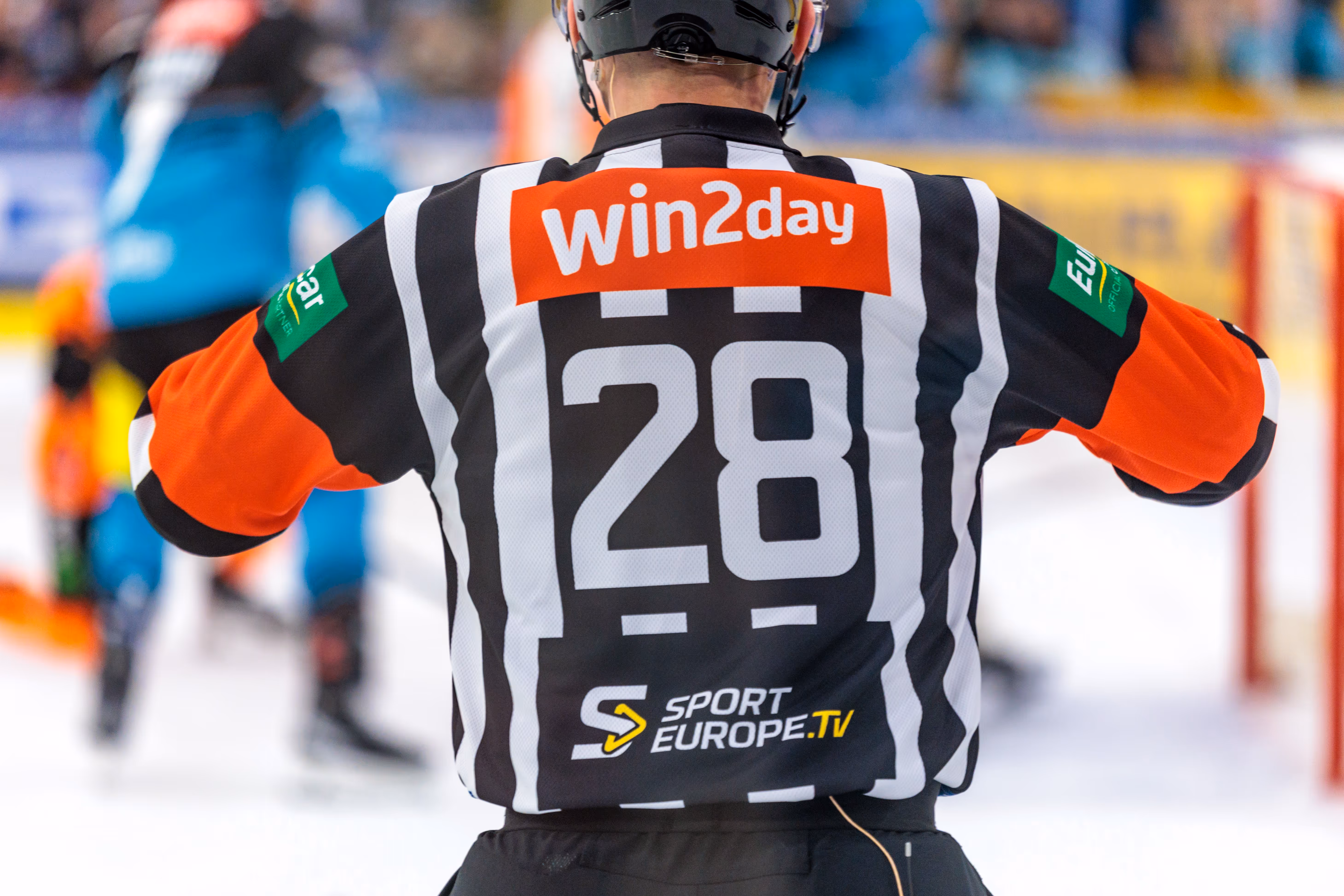 Rückansicht eines Eishockey-Schiedsrichters im schwarz-weiß gestreiften Trikot mit der Nummer 28 und dem Sponsorenlogo von Win2day auf dem Rücken