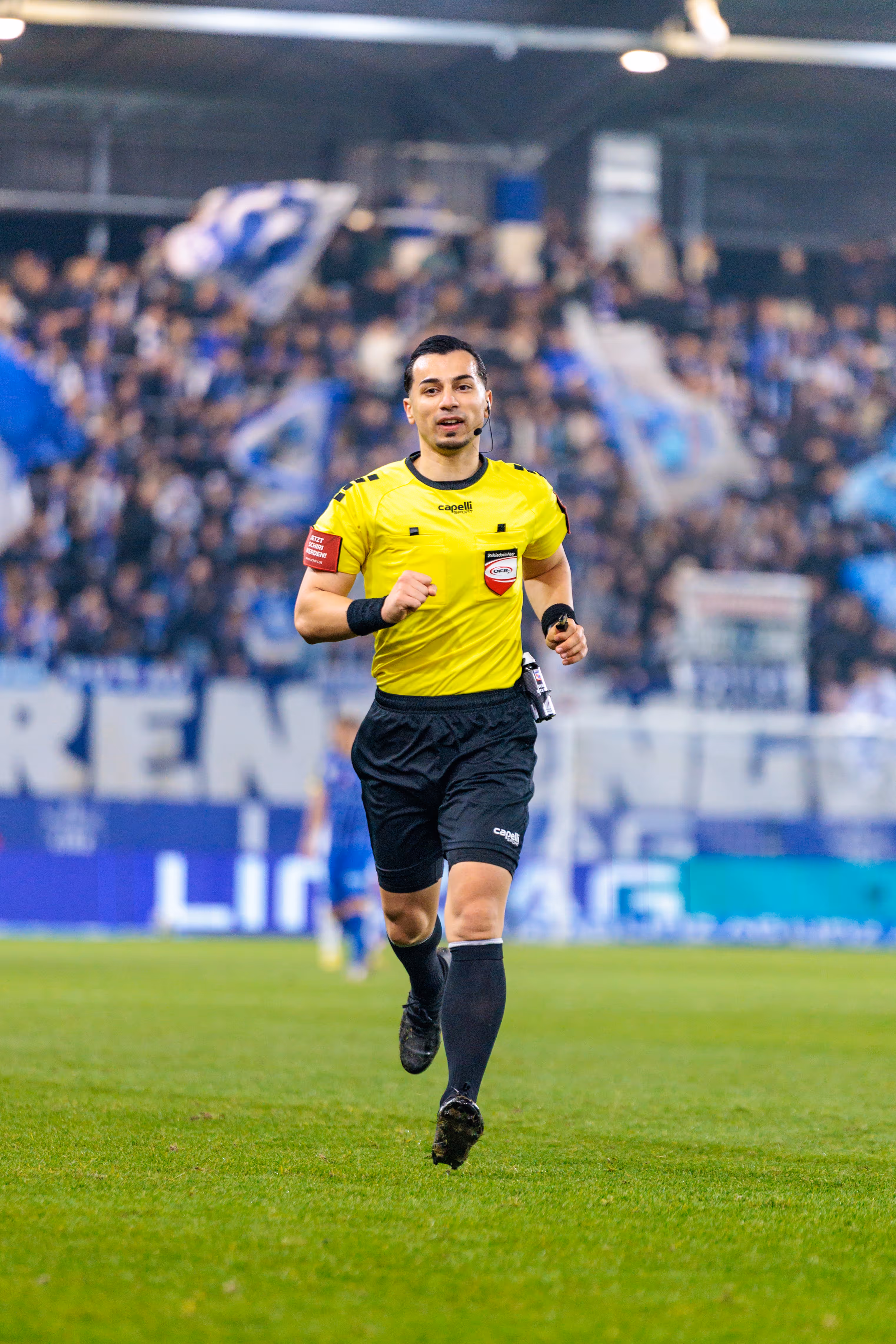 Der Fußball-Schiedsrichter im gelben Trikot und mit Headset läuft konzentriert zum VAR Display während des Linzer Derbys zwischen LASK und Blau-Weiß Linz