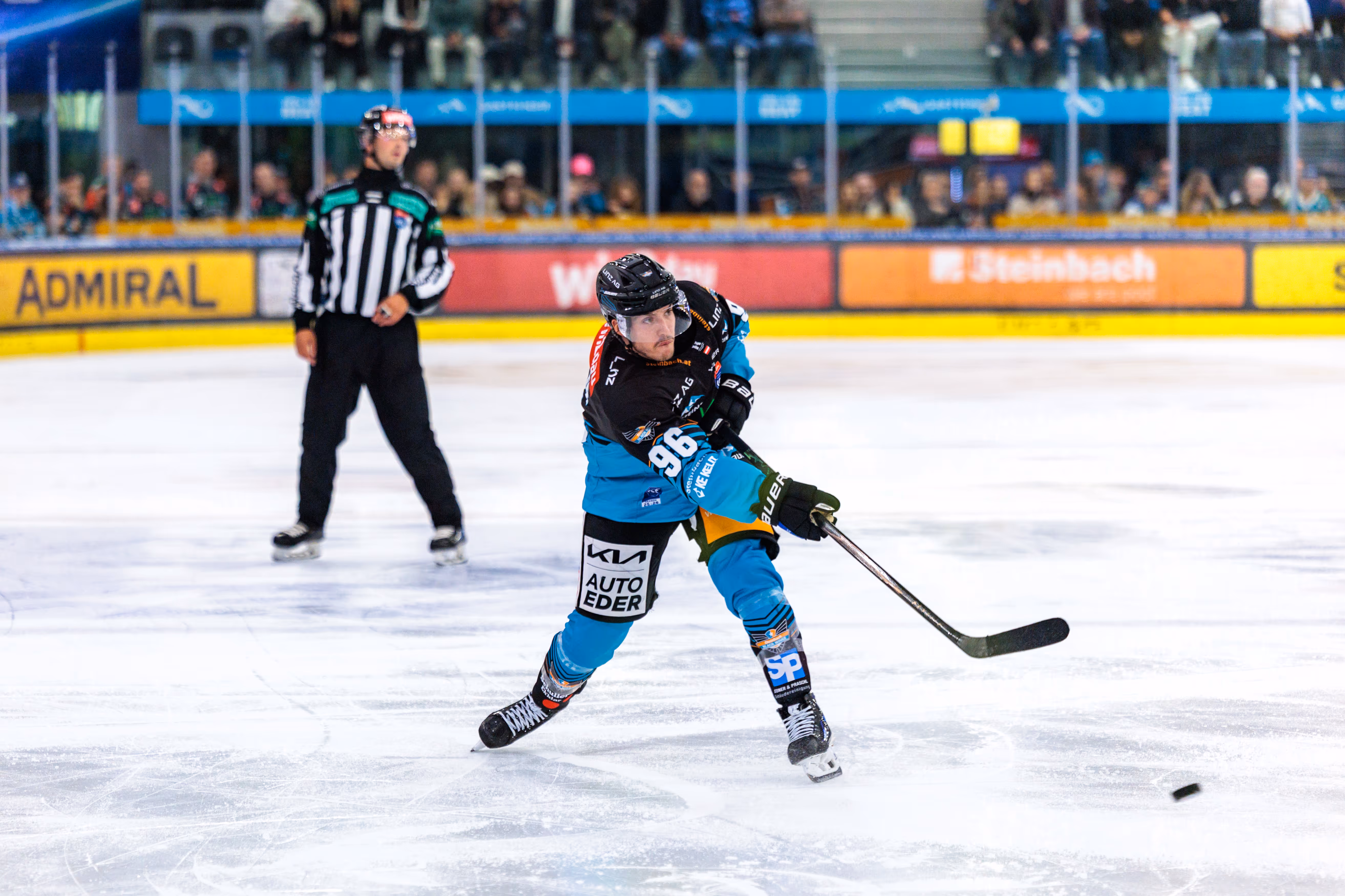 Eishockeyspieler Christoph Tialler in einem schwarz-türkisen Trikot mit der Nummer 96 schießt den Puck auf dem Eis während eines Spiels