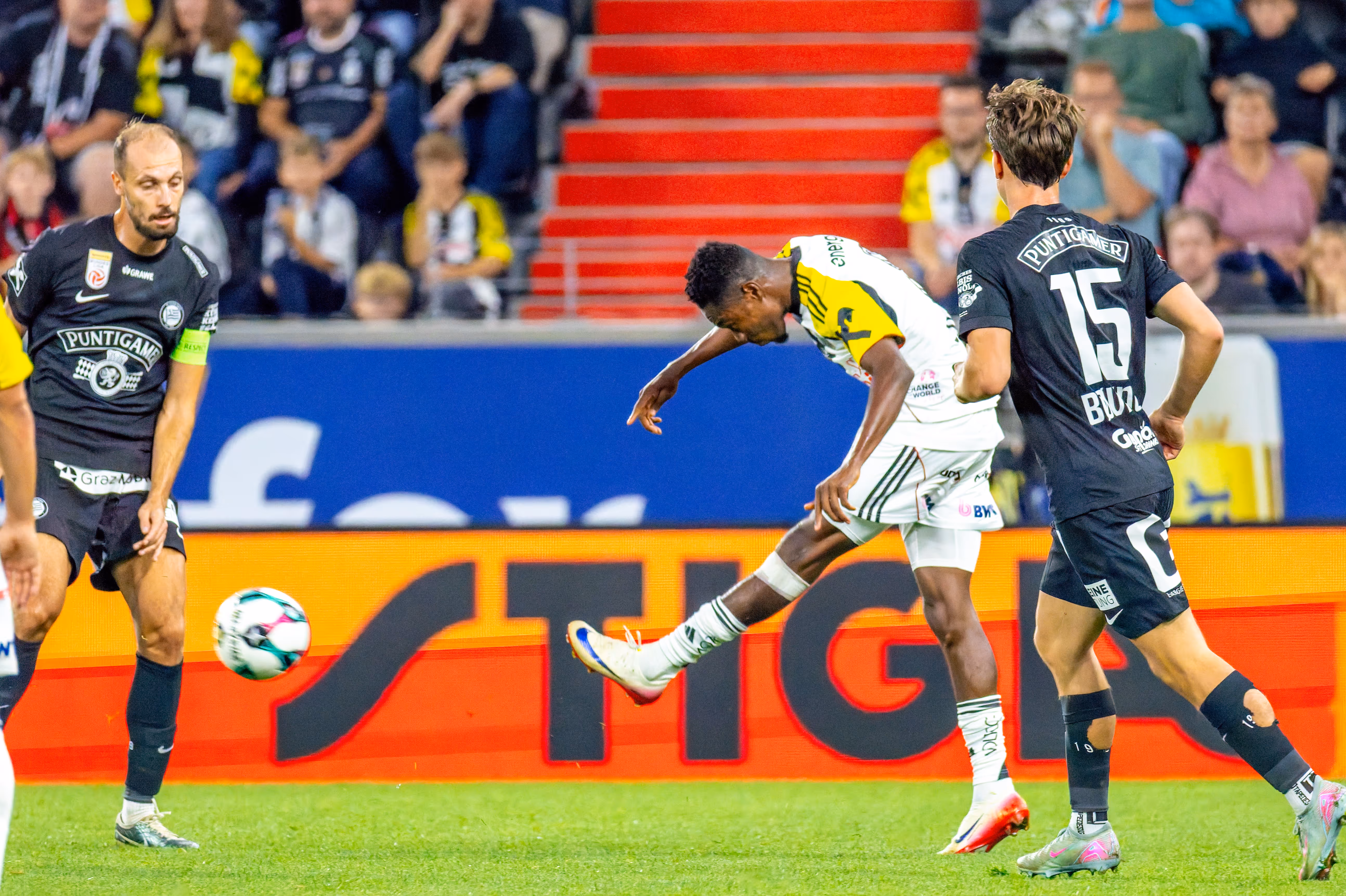 Ein Spieler des LASK schießt den Fußball, umgeben von zwei Spielern des SK Sturm Graz