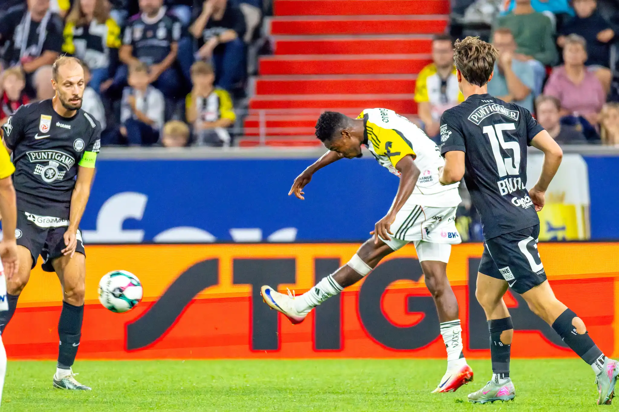 Ein Spieler des LASK schießt den Fußball, umgeben von zwei Spielern des SK Sturm Graz