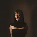Stimmungsvolles Porträt einer jungen Frau mit dunklem, über den Kopf gelegtem Stoff und ernstem Blick