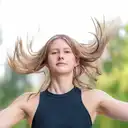 Porträt einer jungen Frau mit dynamisch wehendem blondem Haar und dunklem Oberteil vor einem hellen, unscharfen Hintergrund  lens: 56mm F1.4 DC DN | Contemporary 018