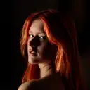 Dramatisches Porträt einer jungen Frau mit leuchtend roten Haaren, die mit intensivem Blick über die Schulter schaut
