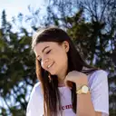 Lächelnde junge Frau mit langen Haaren und goldener Uhr in weißem T-Shirt vor unscharfem Naturhintergrund  lens: Viltrox AF 23/1.4M