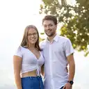 Porträtfoto von einem lächelnden jungen Mann und einer jungen Frau, die im Freien vor einem sonnenbeschienenen, unscharfen Grün stehen  lens: 56mm F1.4 DC DN | Contemporary 018