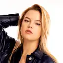 Nahaufnahme-Porträt einer selbstbewussten jungen blonden Frau in einer schwarzen Lederjacke mit goldenen Creolen und einer S-Halskette vor weißem Hintergrund  lens: 56mm F1.4 DC DN | Contemporary 018