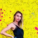 Eine junge Frau mit blonden Haaren und blauen Augen posiert vor einer leuchtend gelben, strukturierten Wand mit pinken Farbspritzern  lens: 56mm F1.4 DC DN | Contemporary 018